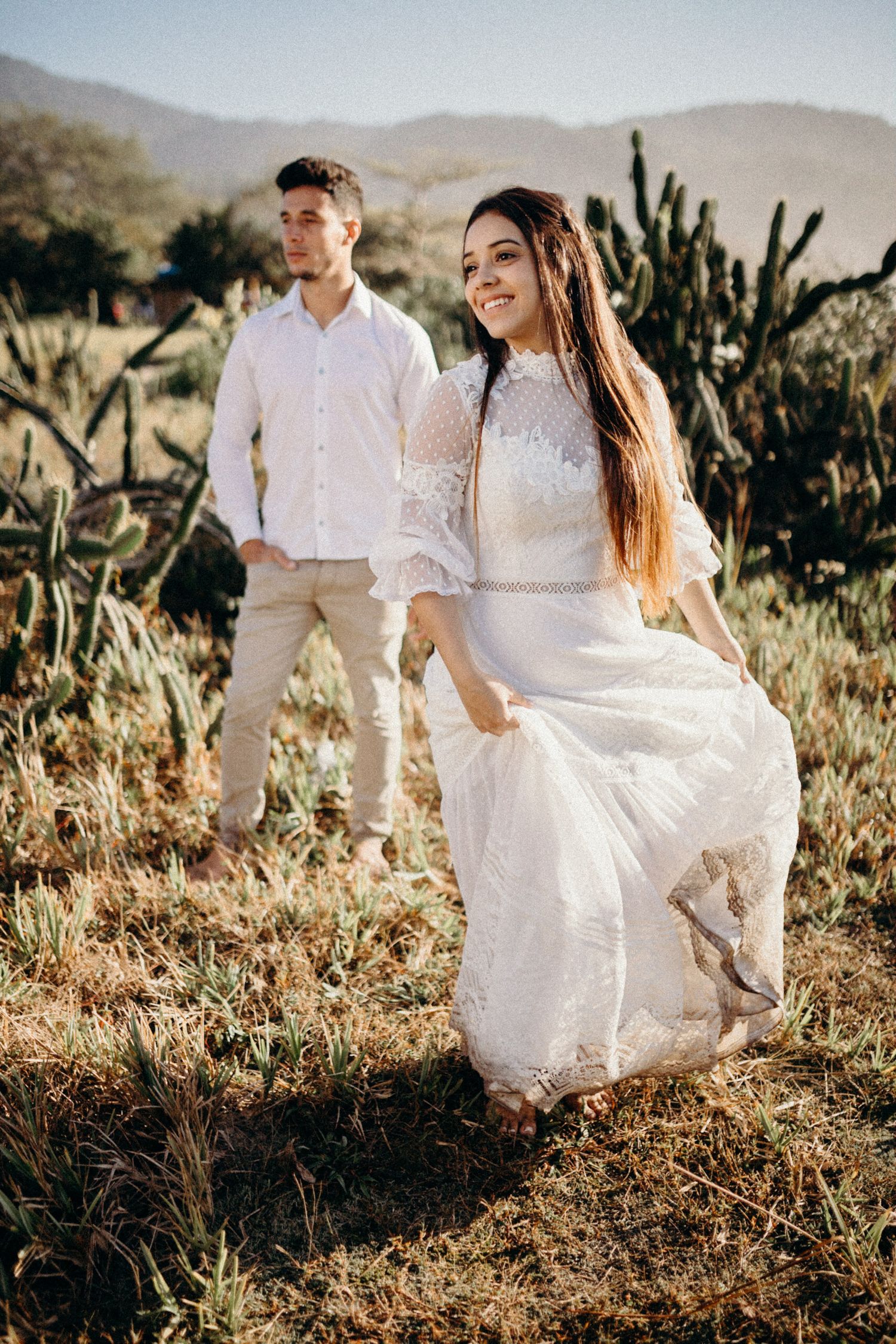 Desert engagement photo with bride twirling white dress among mountain scenery.