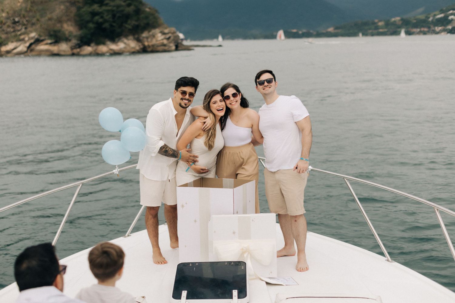 A group celebrating on a boat deck with light blue balloons against a coastal backdrop.