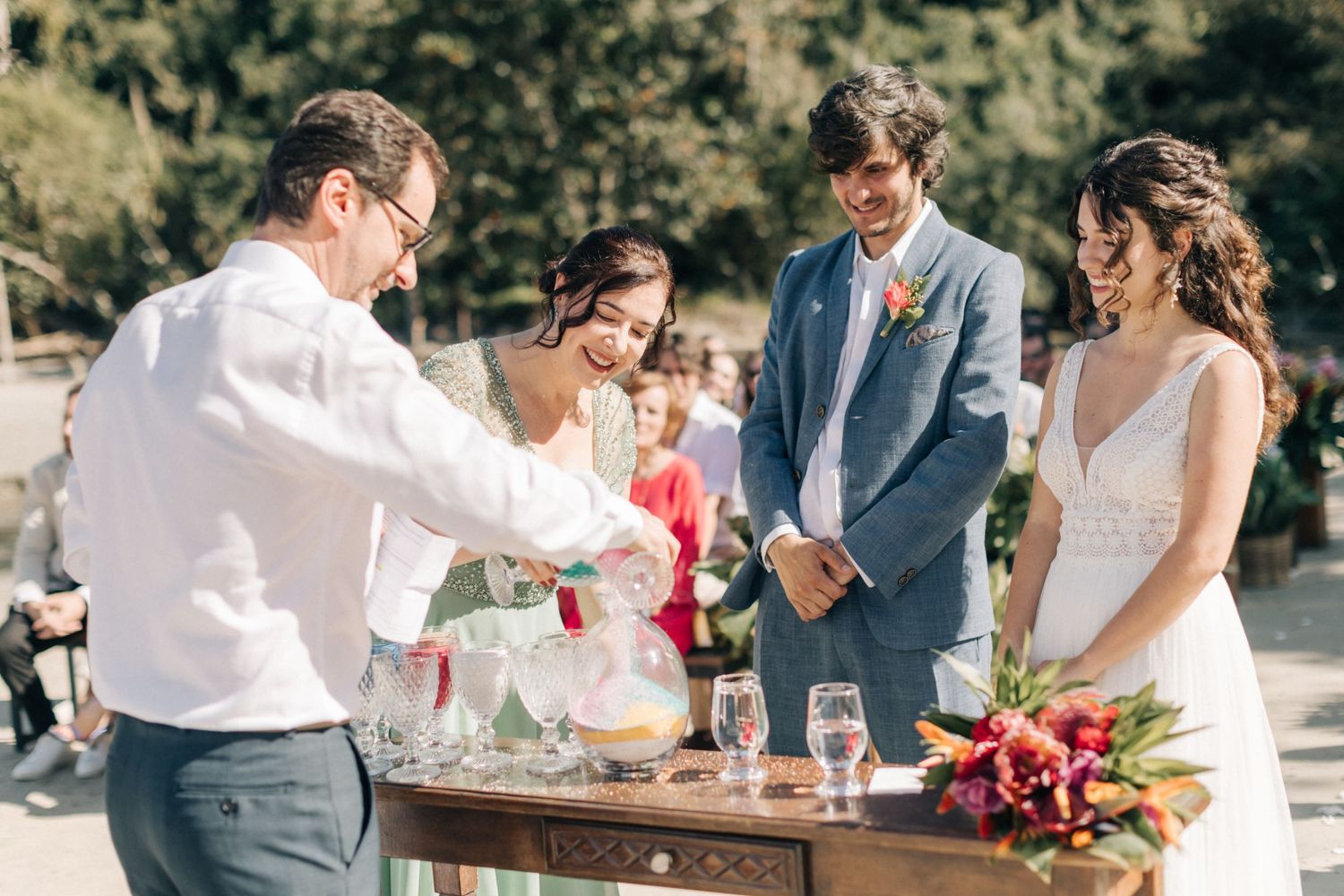 Wedding party gathers around drink mixing station during outdoor celebration.