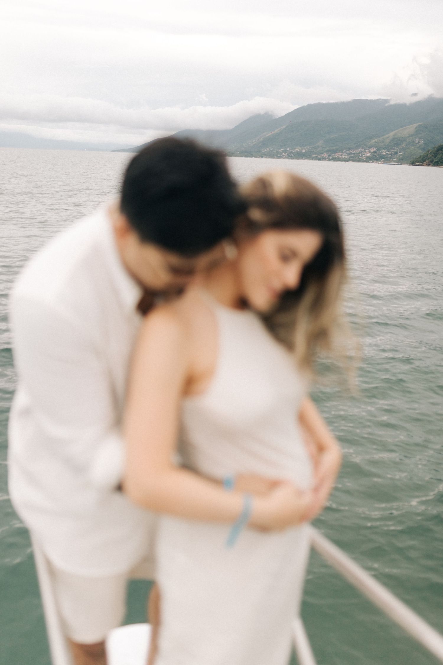 Intimate embrace captured on boat deck with mountains and lake in soft focus.
