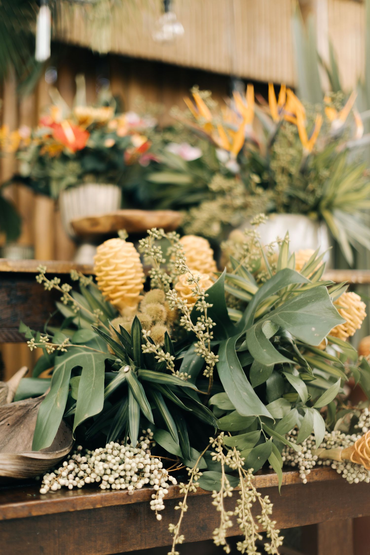 Tropical floral arrangement featuring banksia flowers and greenery on wooden display.