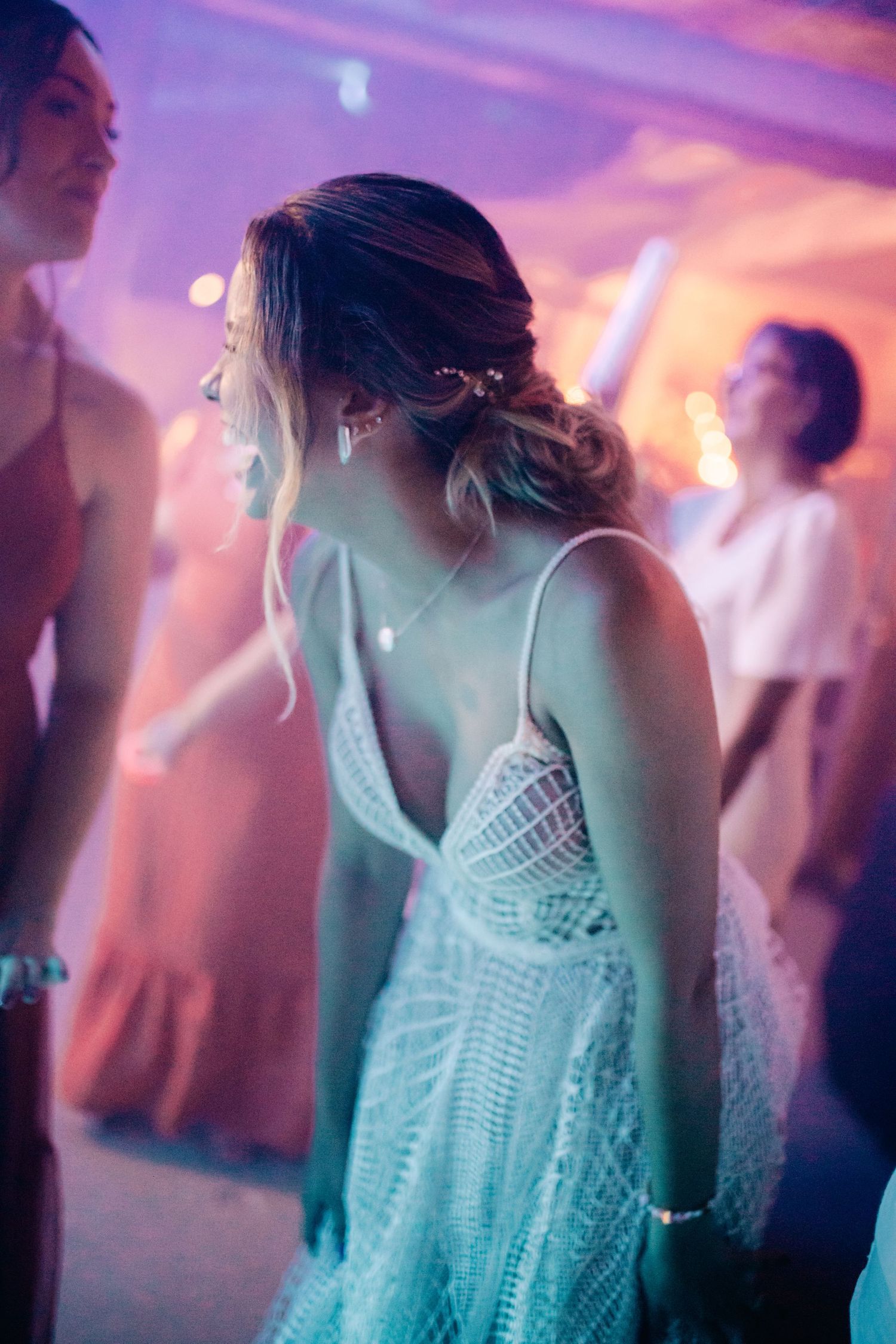 Dancing guest in a lace dress under purple and pink reception lighting.