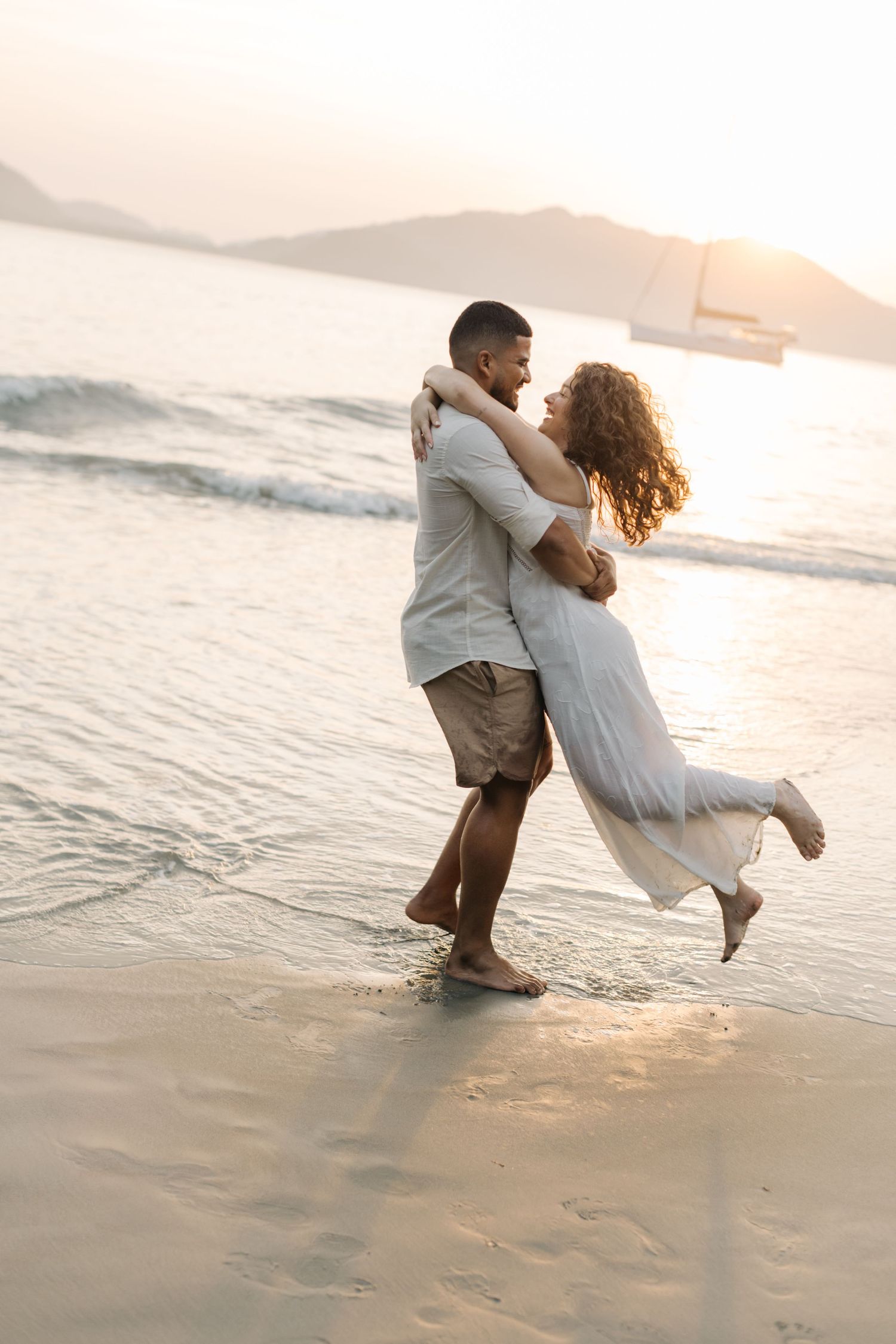 Couple dancing and laughing in ocean waves during golden hour photography session.