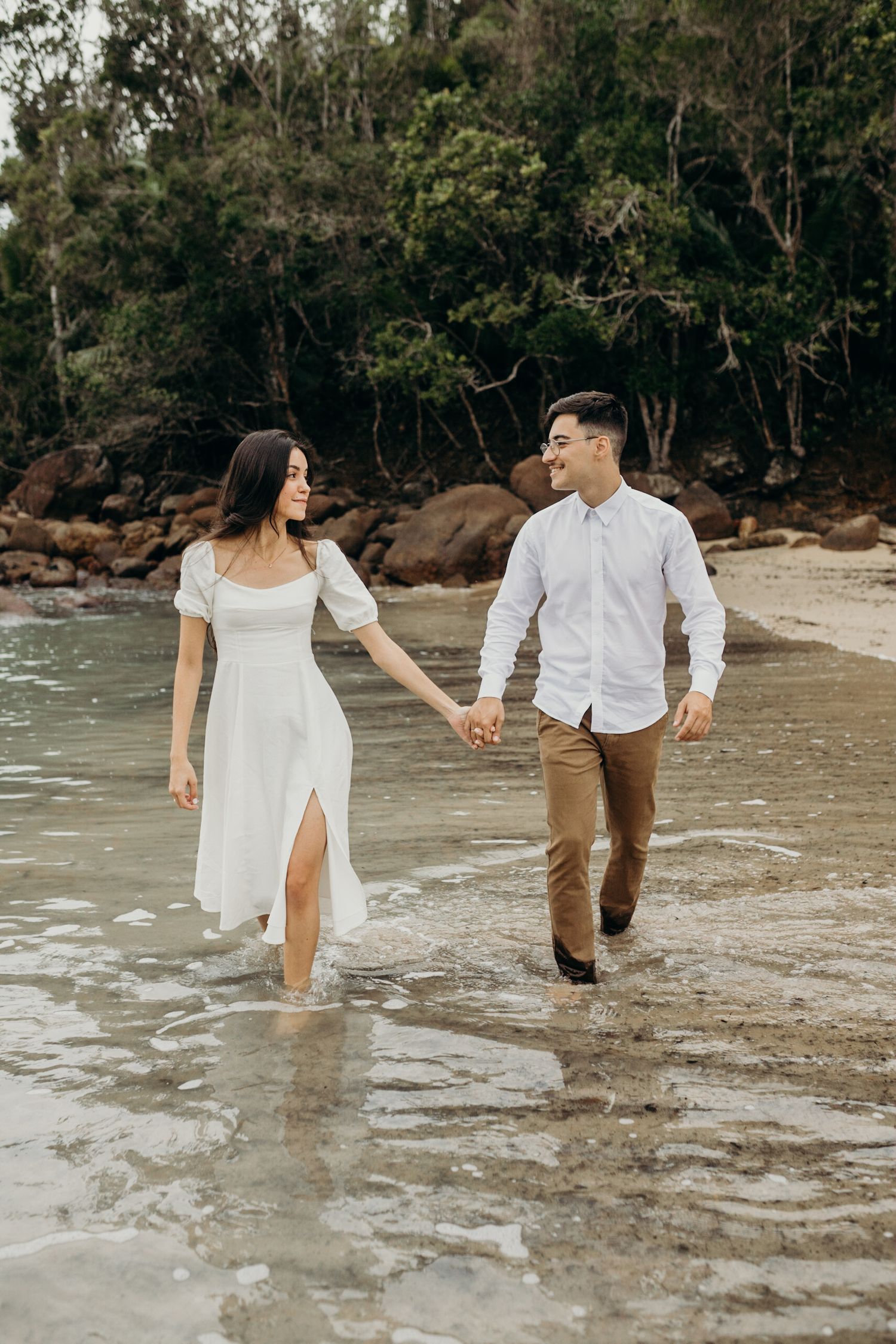 A couple splashes through shallow ocean waves during their beach photography session.