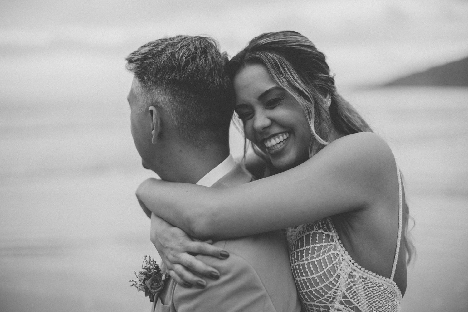 A romantic black and white portrait captures a couple embracing on a beach.