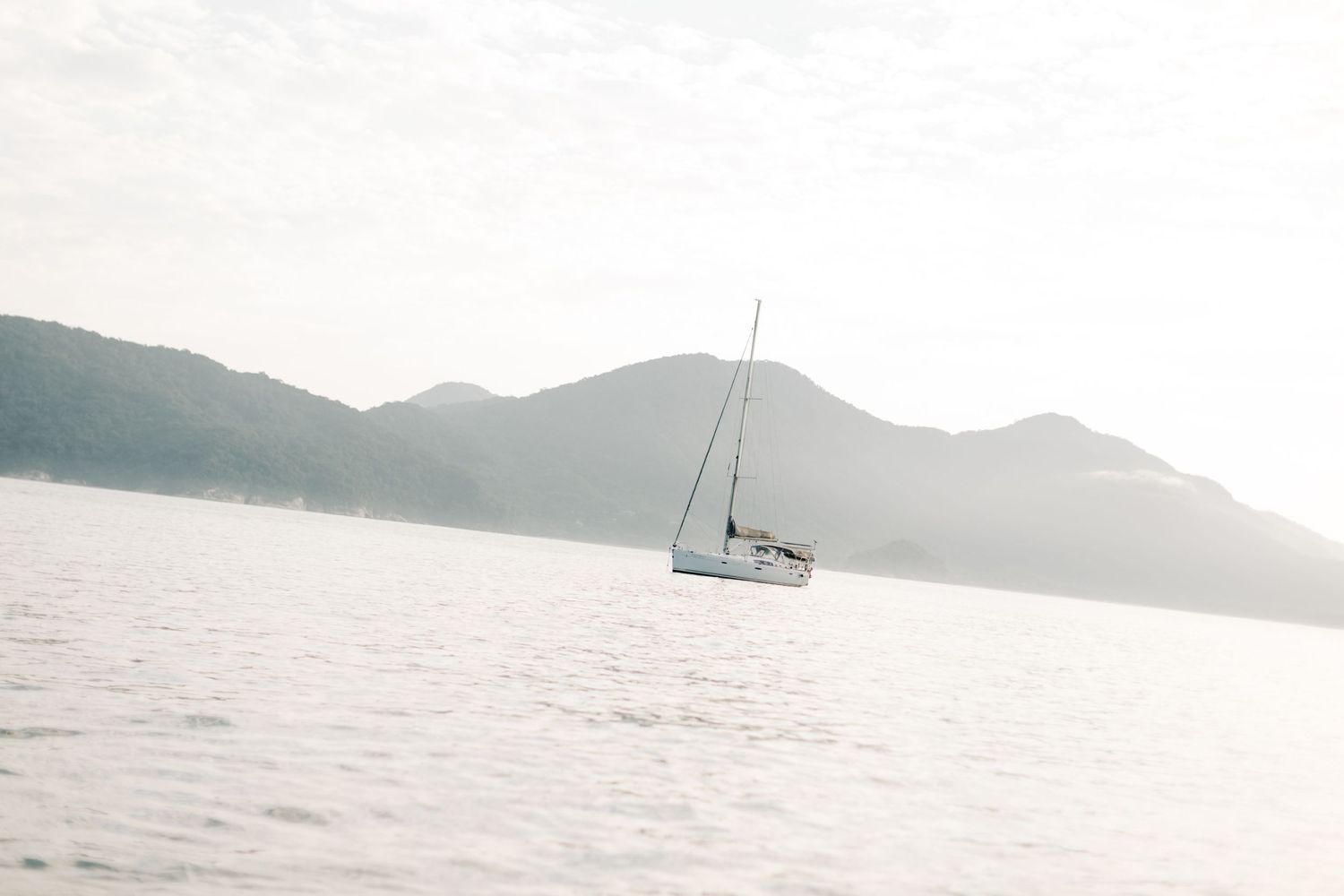 A lone sailboat anchored in tranquil waters against a mountainous backdrop.