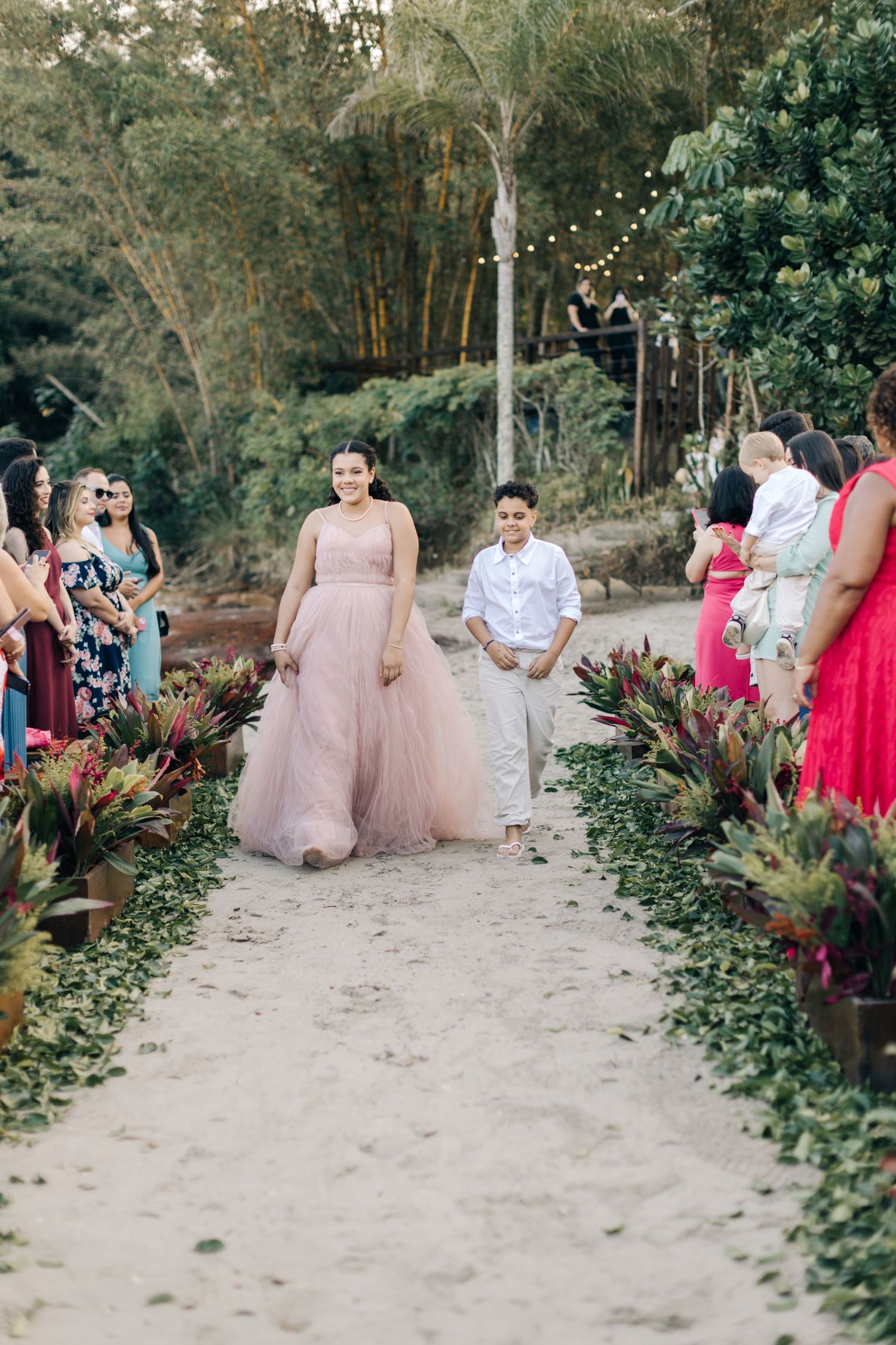 Wedding processional on garden path with guest in flowing pink tulle gown.