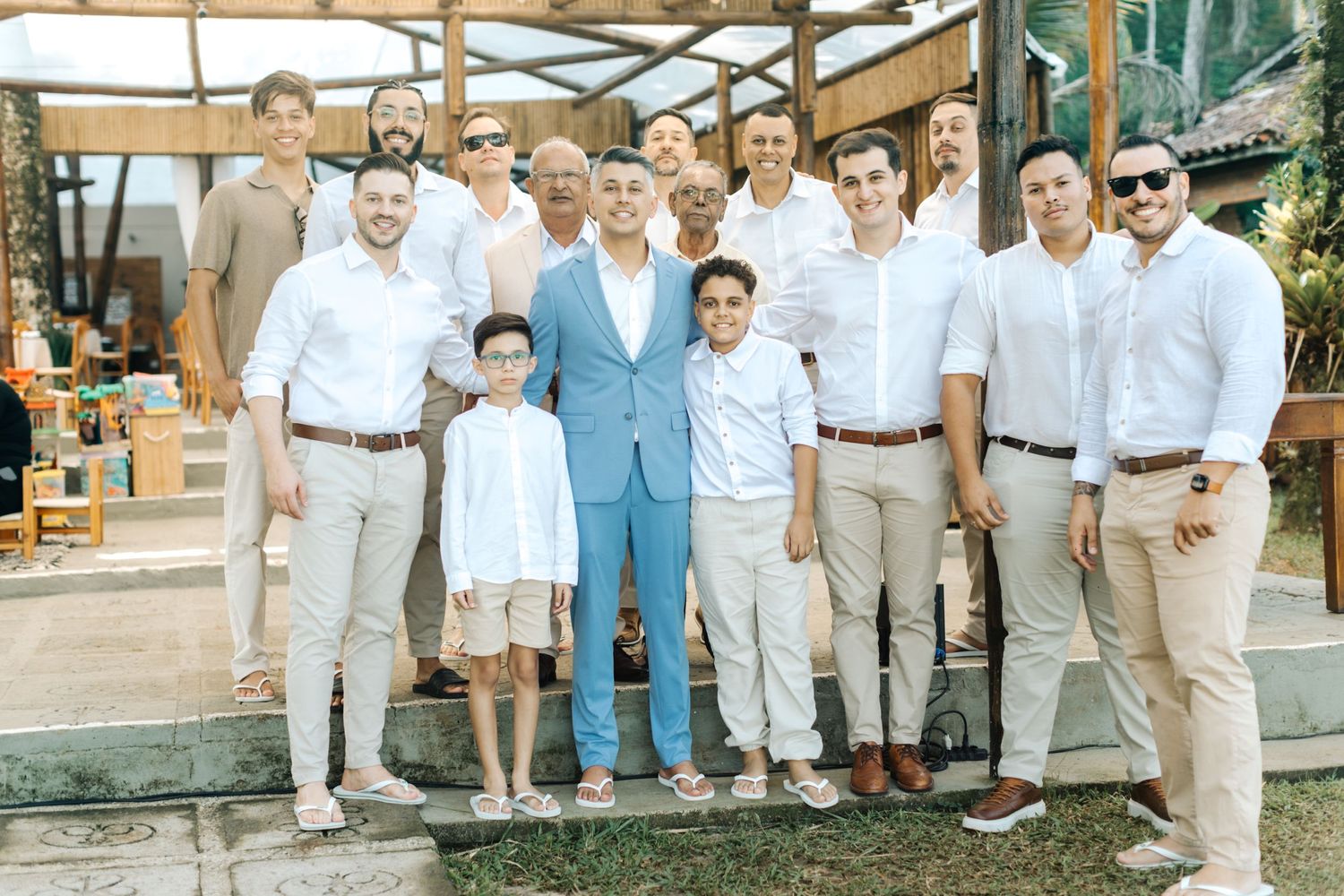 Group photo of wedding party members dressed in light colored suits and formal attire.