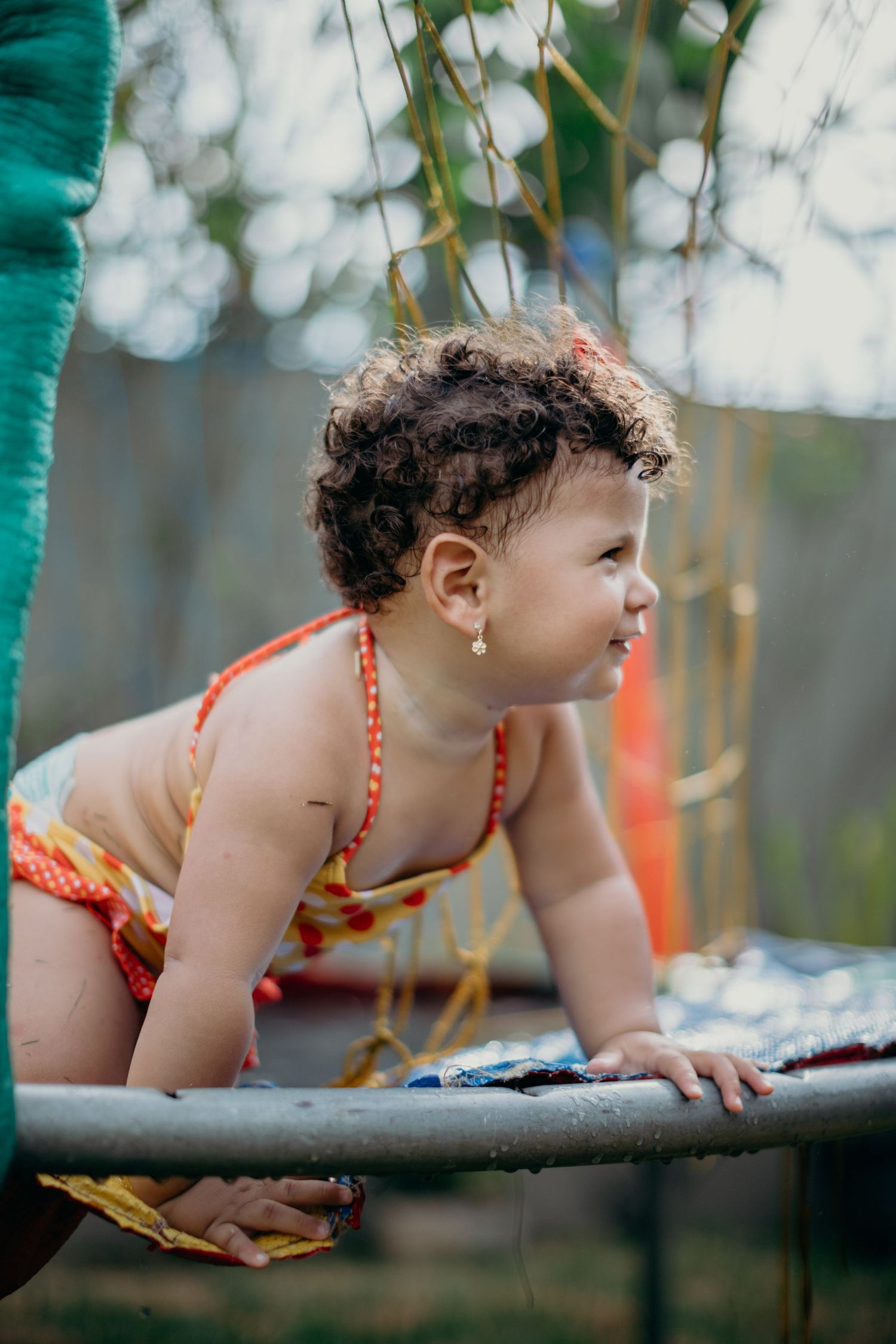 Child in orange swimwear leaning forward against teal surface during summer play.