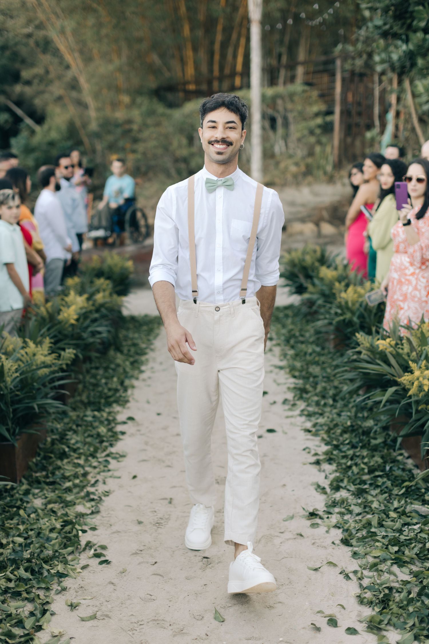Wedding guests in white attire and casual wear walk along a garden path.