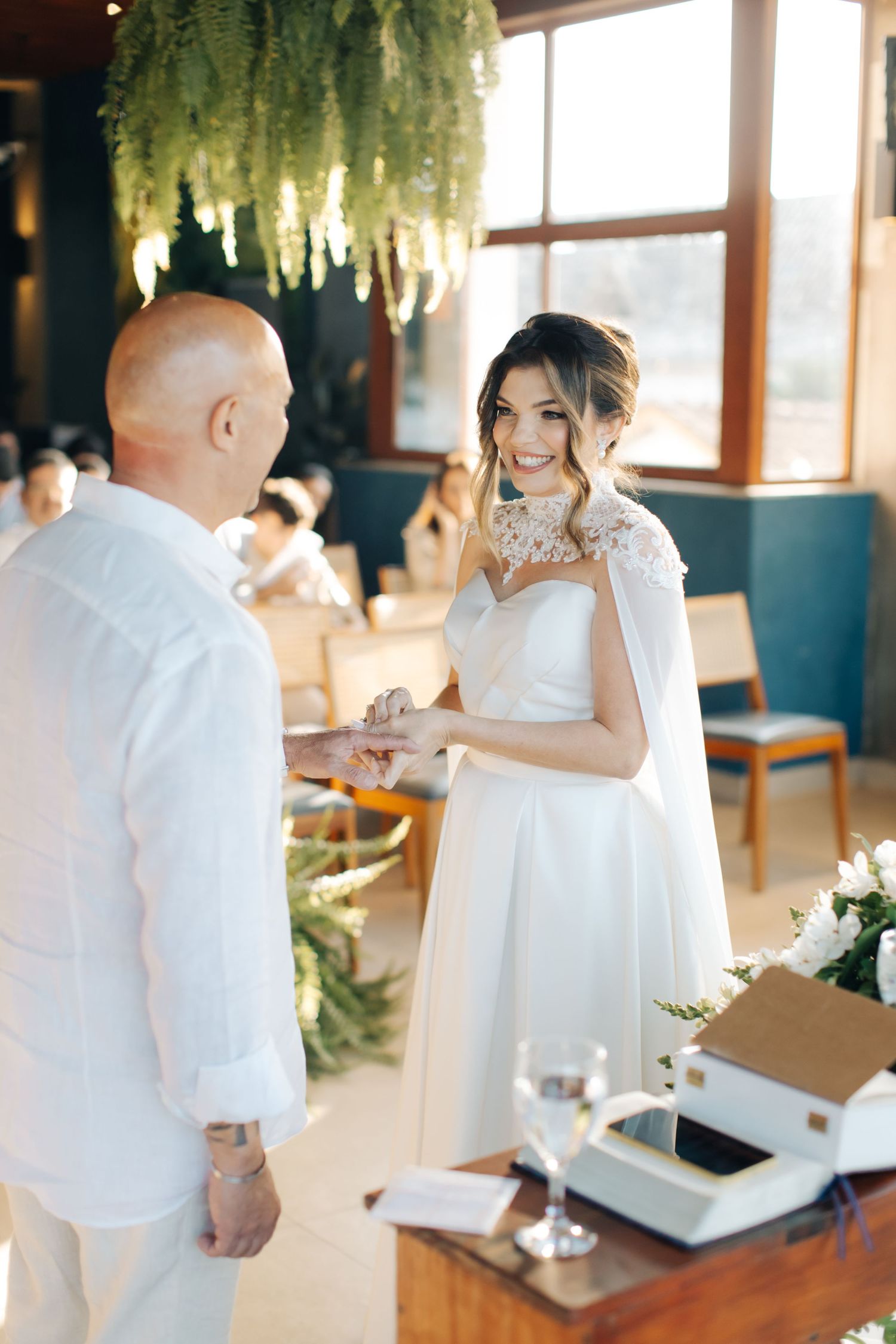 A tender moment during a wedding ceremony with hanging plants and natural light streaming through windows.