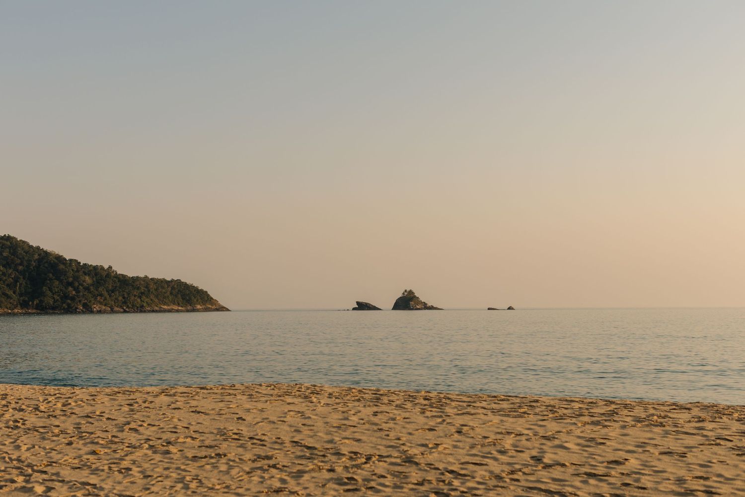 Panoramic view of a serene tropical beach with distant islands on the horizon during golden hour.