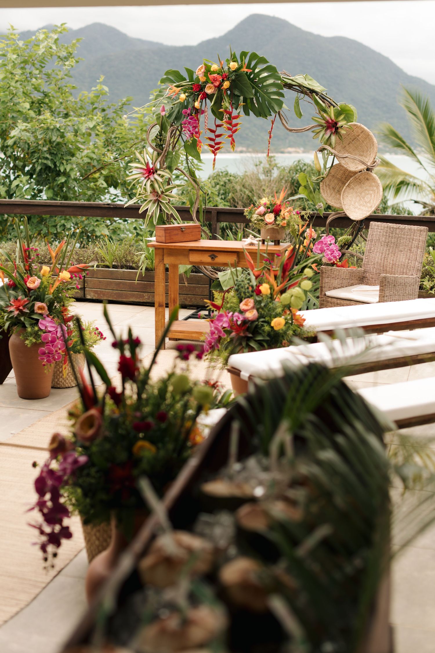 Tropical floral arrangements with vibrant red and pink flowers decorate an outdoor venue with mountain views.