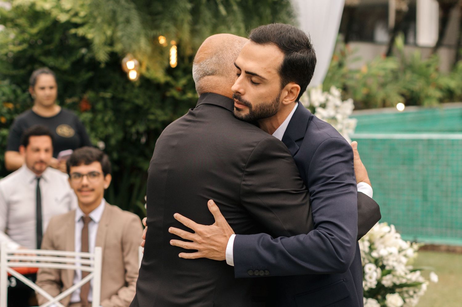 Wedding guests embrace in an emotional moment during an outdoor ceremony celebration.