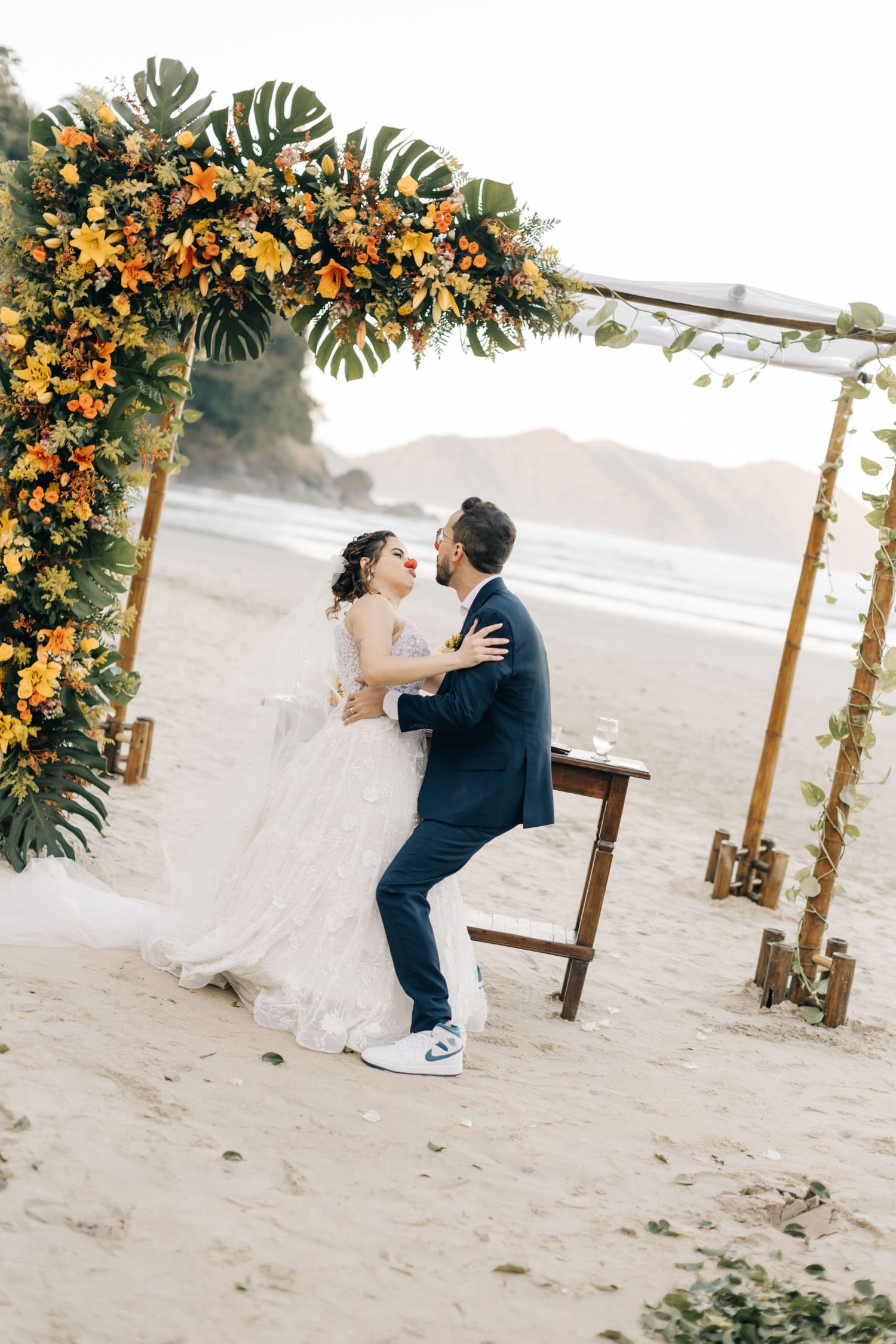 A joyful wedding dance captured on a scenic beach with mountains and floral decorations.