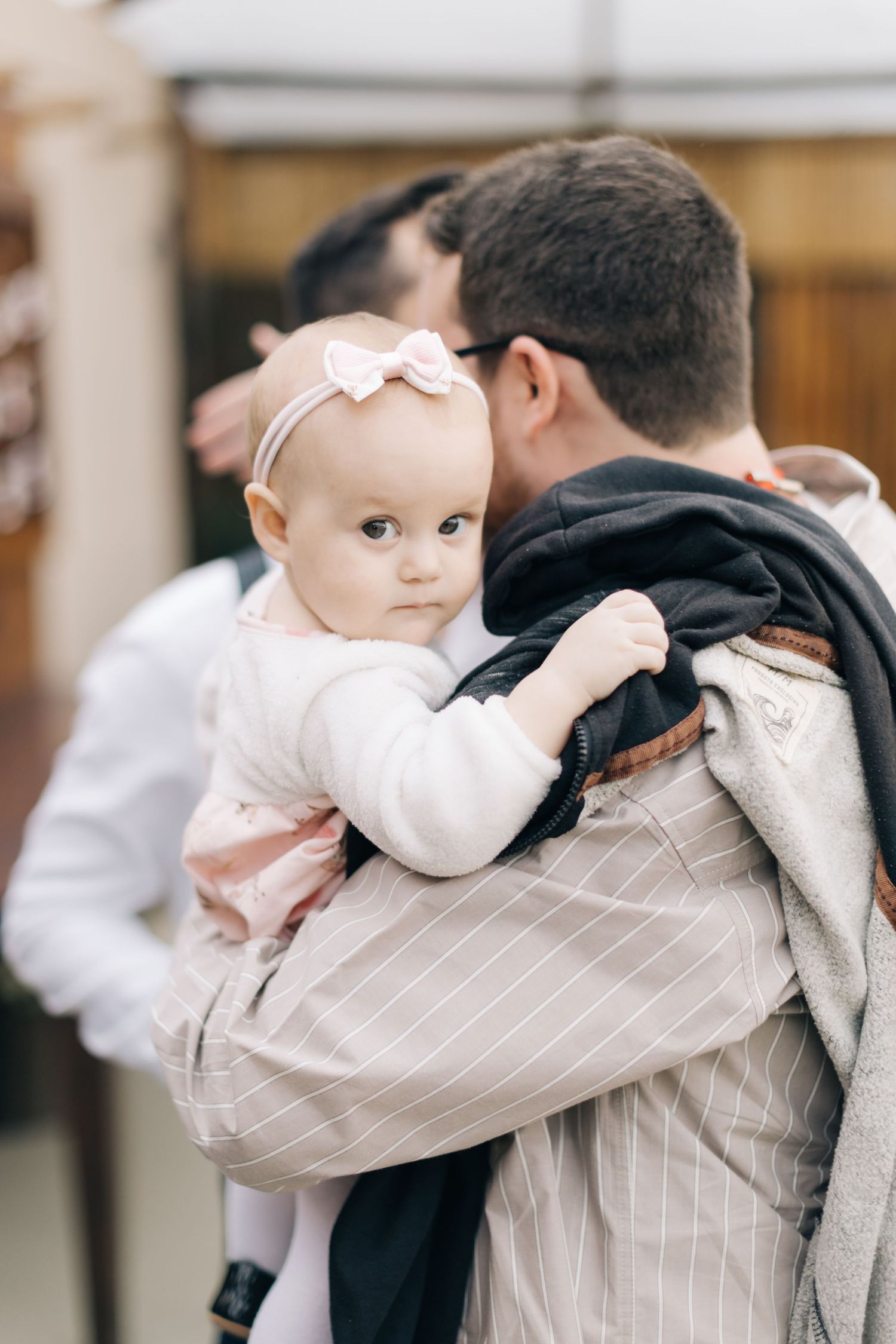 Baby in white dress being held during special occasion.