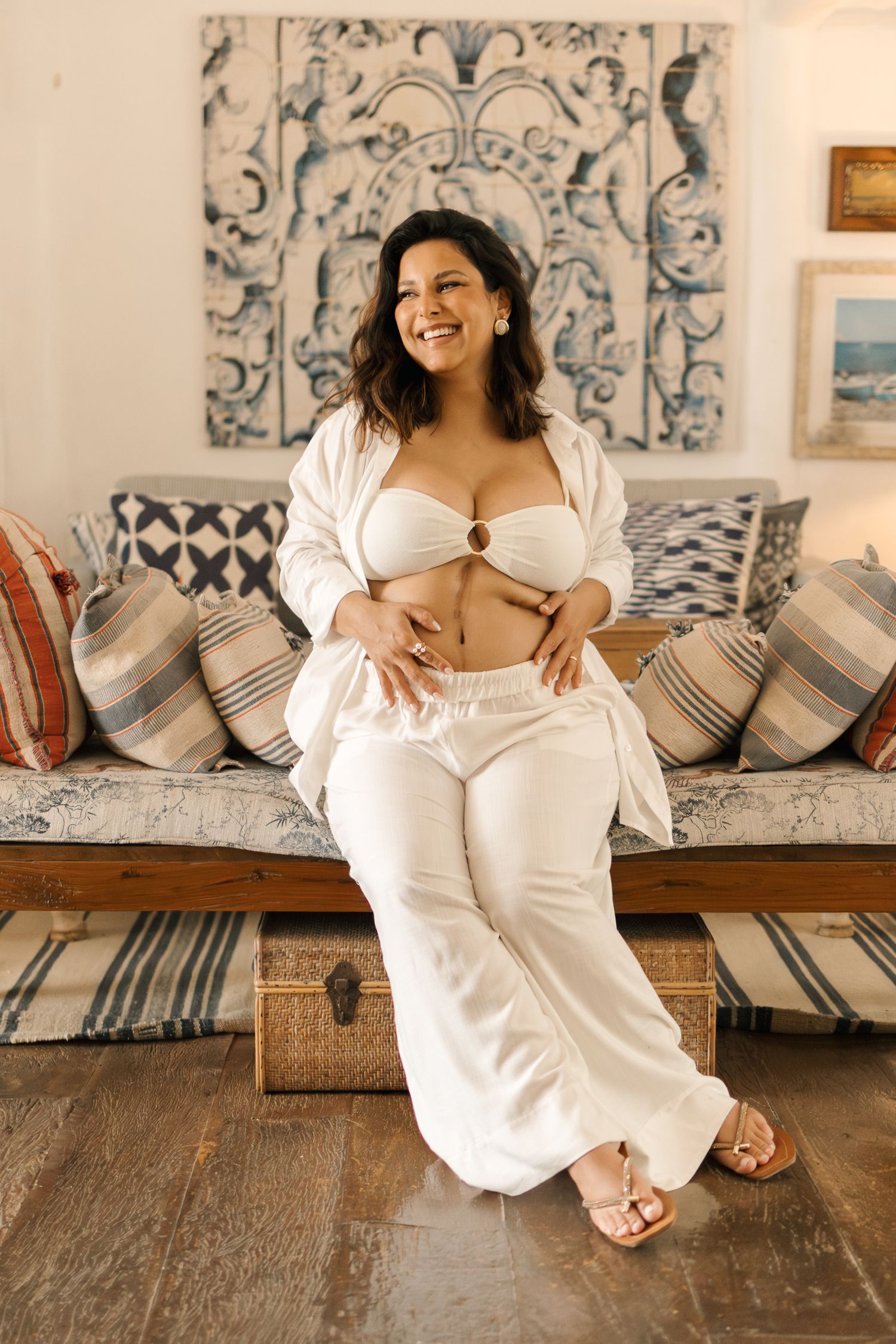A person in a white dress lounges on a couch with blue and white striped pillows against an ornate patterned wall.