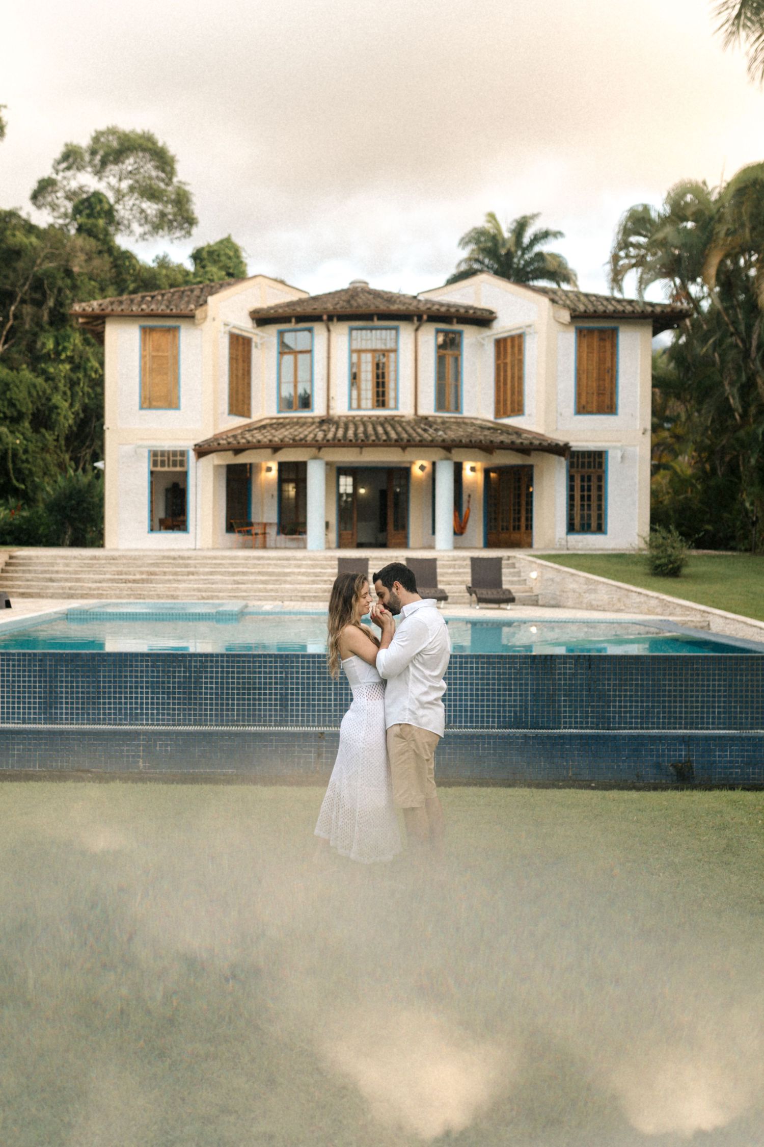 A romantic moment captured in front of a luxury white house with a swimming pool.