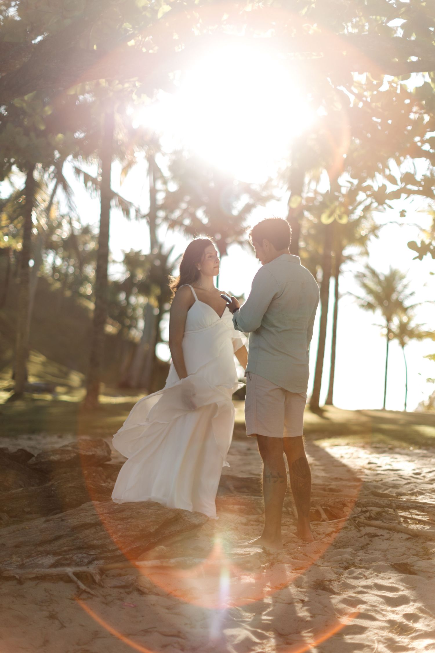 A romantic beach photoshoot at sunset with palm trees silhouetted in the background.