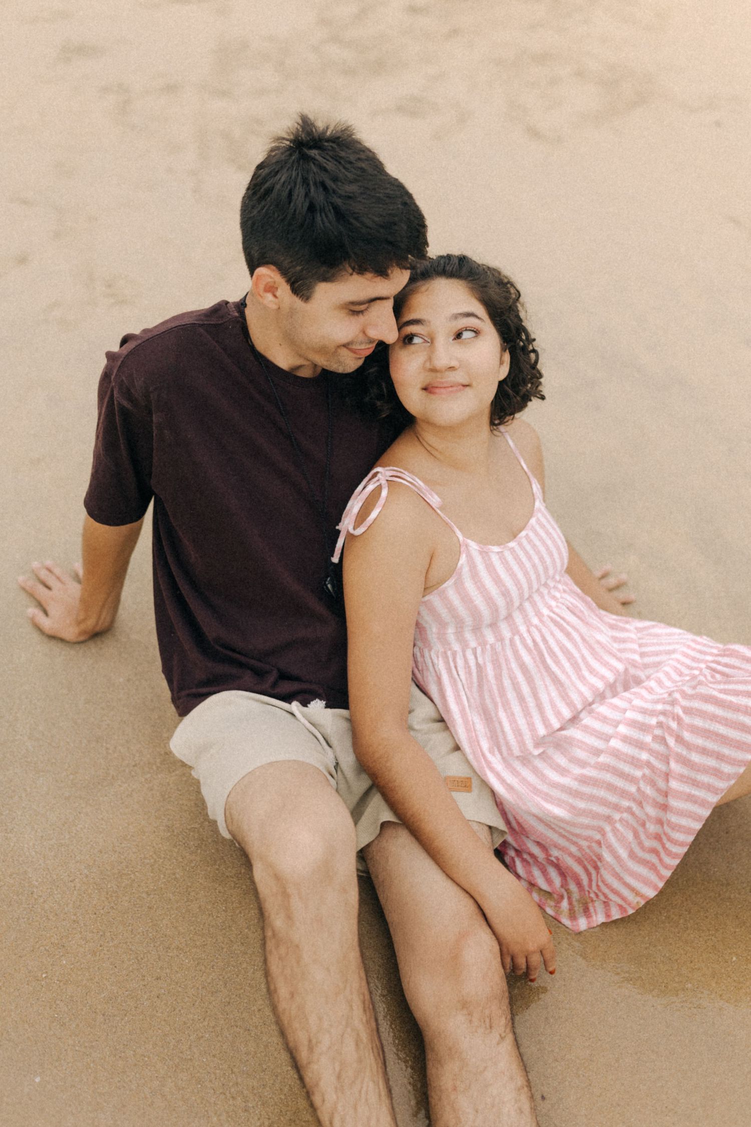Um casal relaxa junto em uma superfície de areia, vestindo roupas casuais de verão em listras marrons e rosa.
