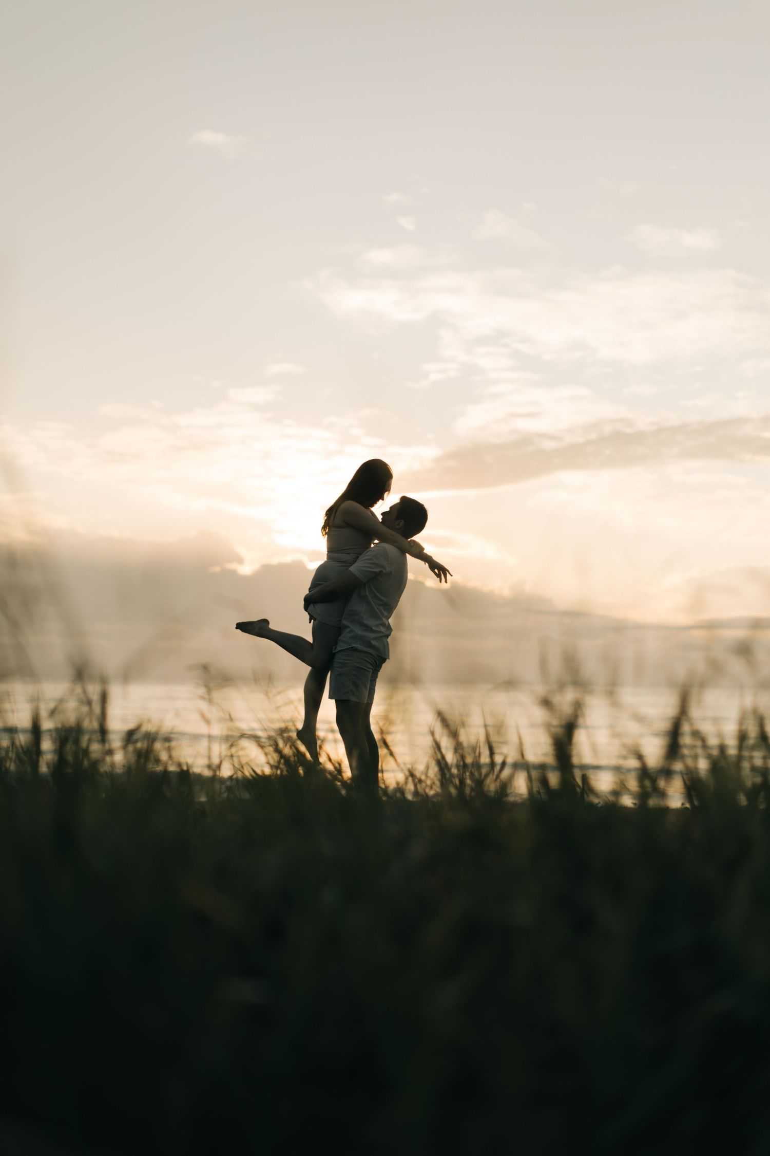 Silhouetted couple embraces in a romantic sunset moment against a misty landscape background.