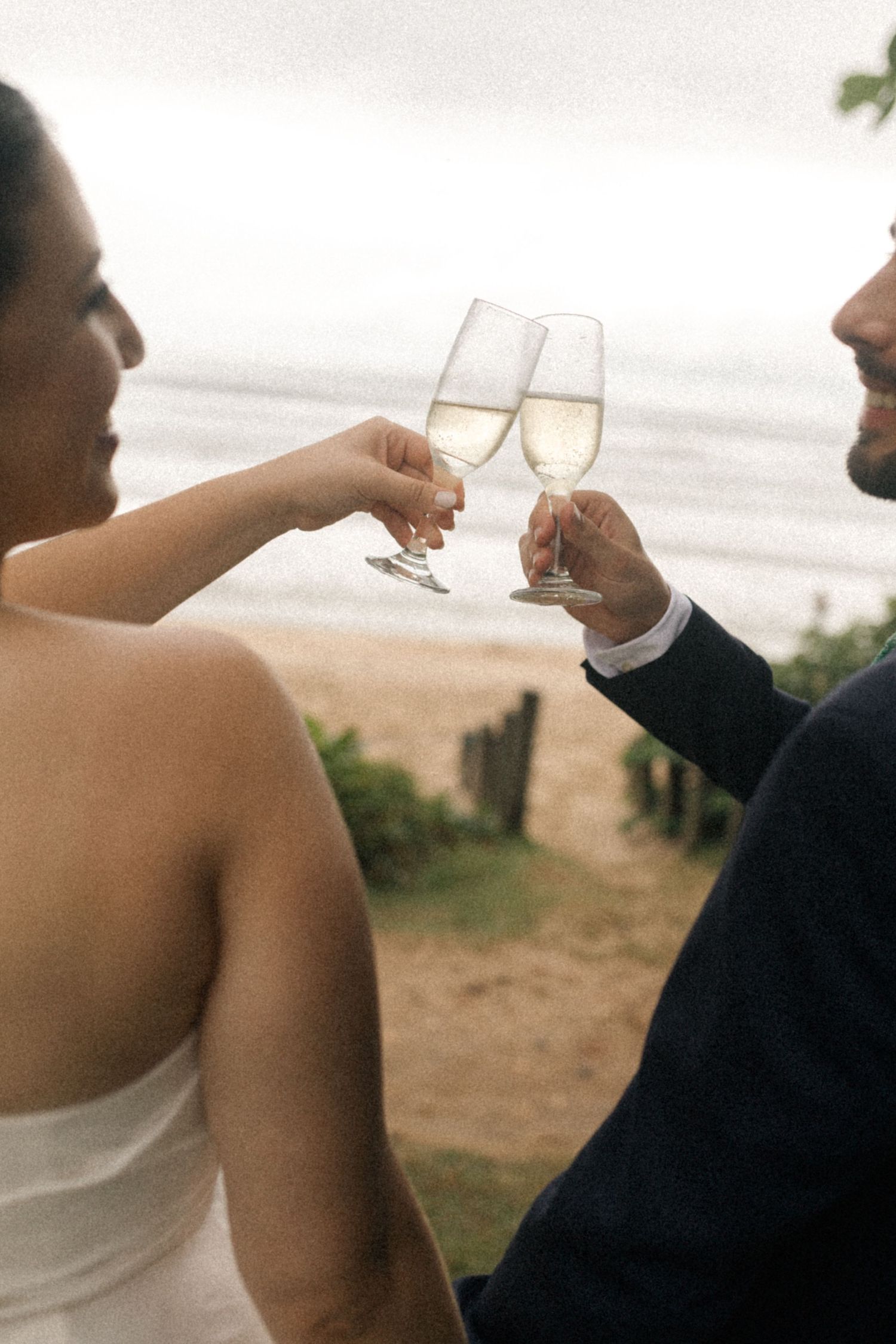 A couple toasts with champagne glasses at a beachside wedding venue.