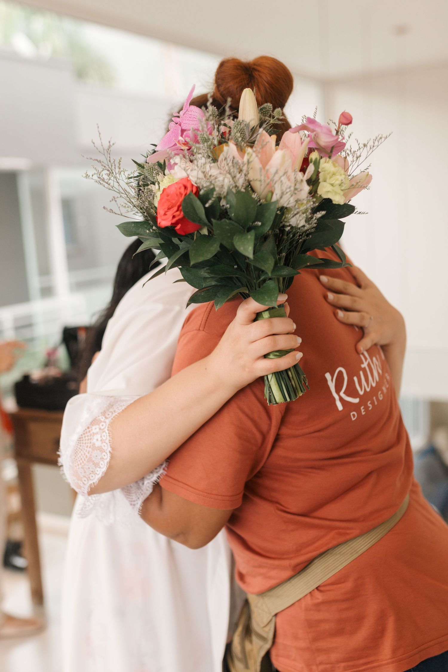 Two people embracing with a colorful bouquet of pink and coral flowers between them.