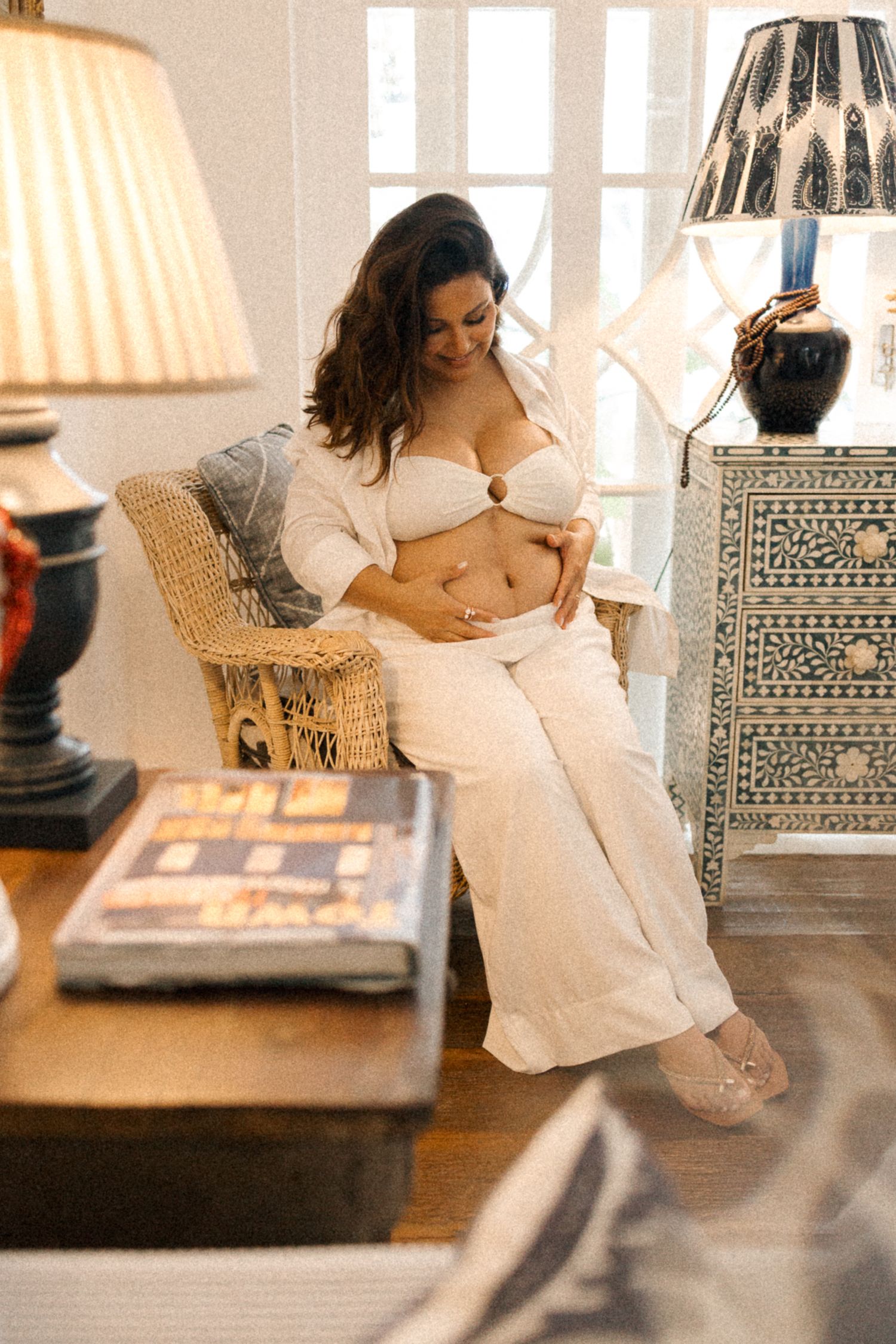 A series of intimate maternity photos showing a woman in white sitting on a couch in a sunlit room with patterned furniture.