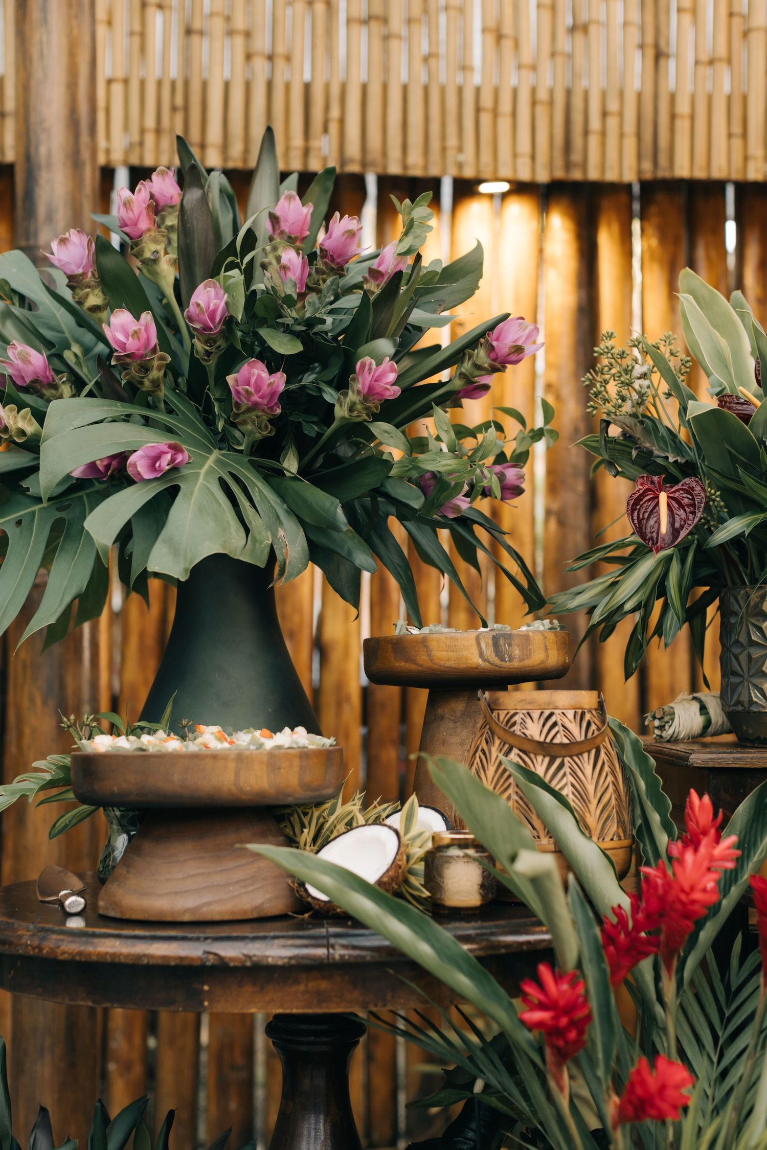 Tropical floral arrangements with pink and red blooms against bamboo backdrop.