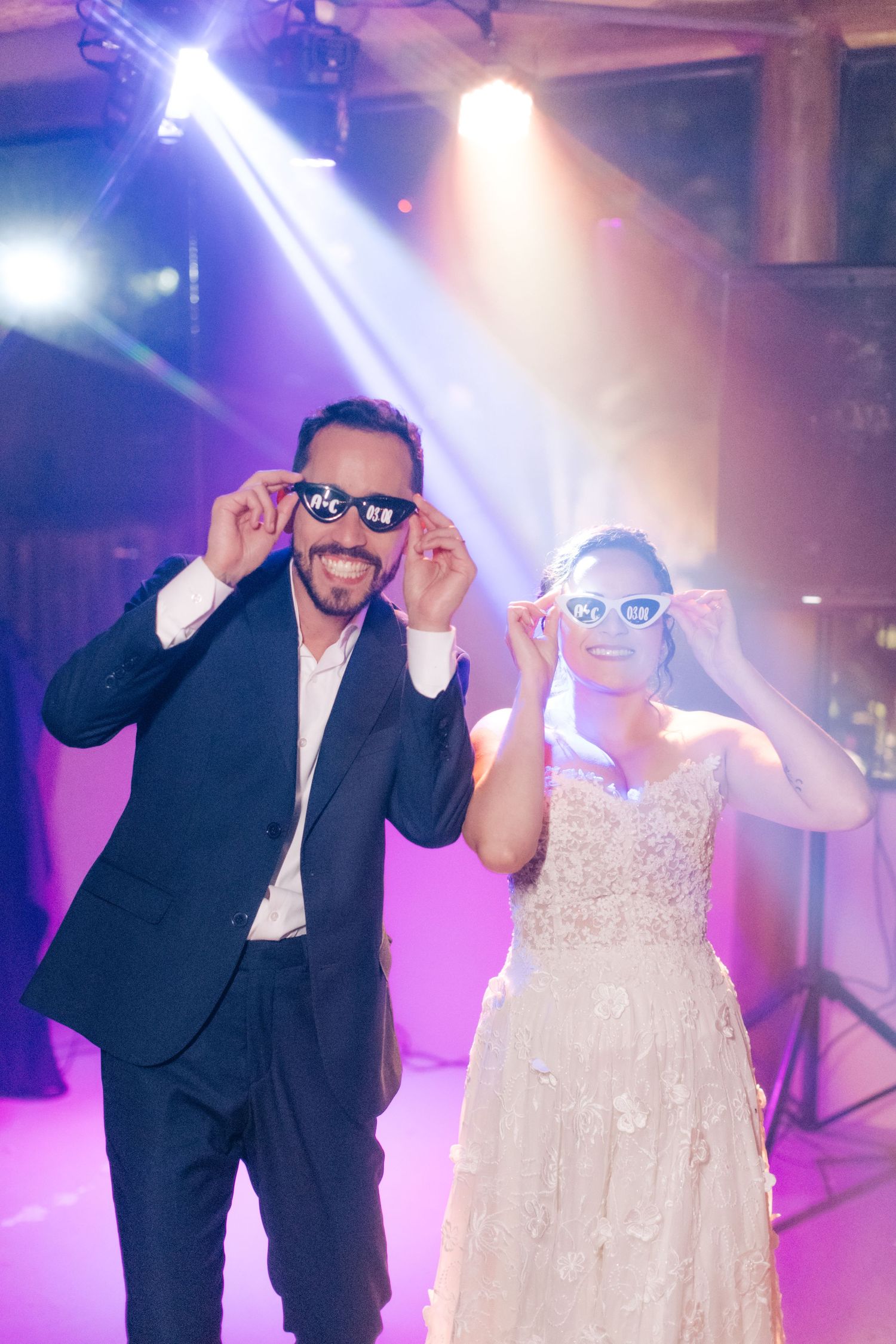 A fun wedding reception moment with matching sunglasses and purple lighting on the dance floor.