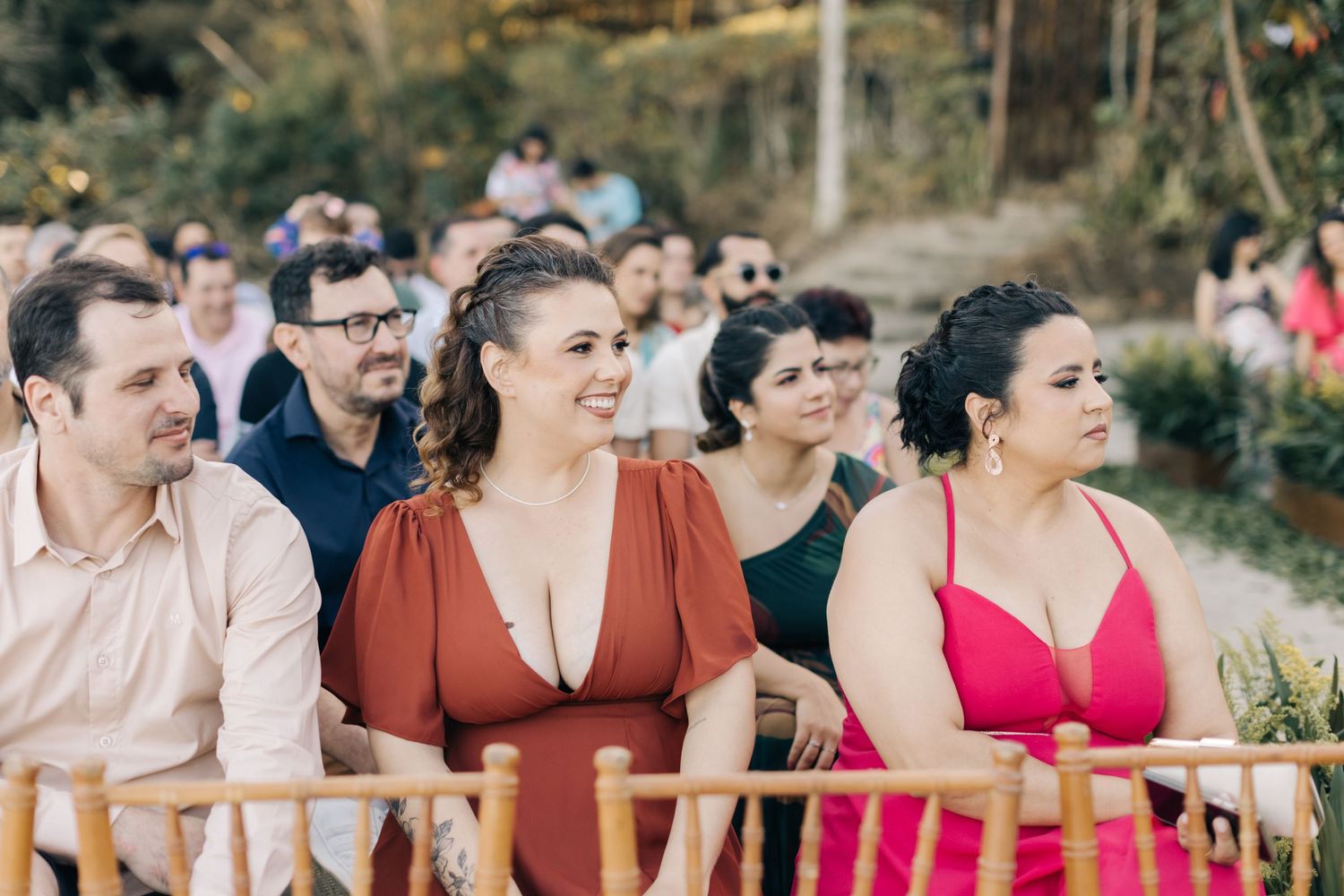 Wedding guests seated in chairs smiling during an outdoor ceremony.