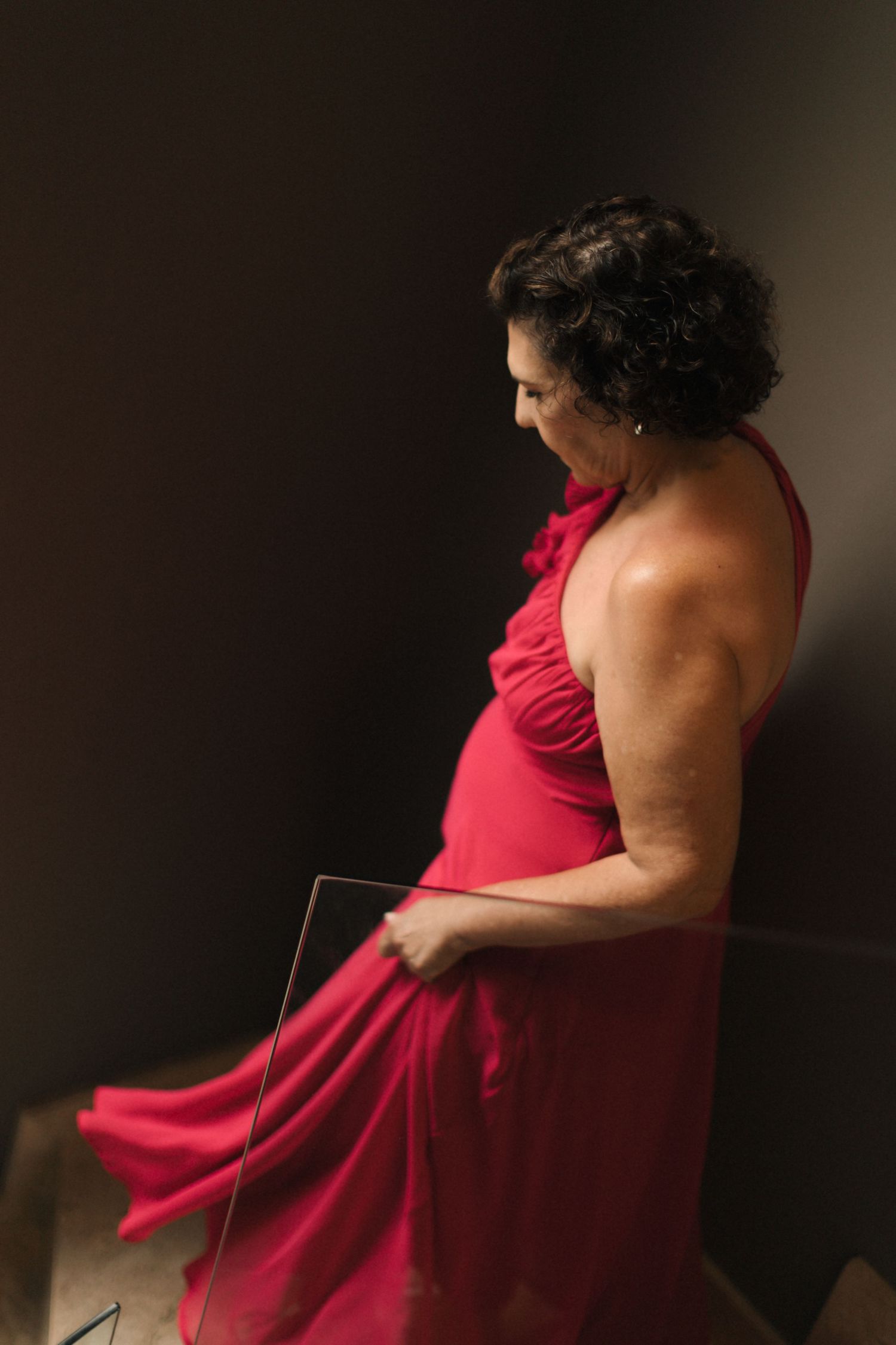 Side view of person in flowing red formal dress against dark background.
