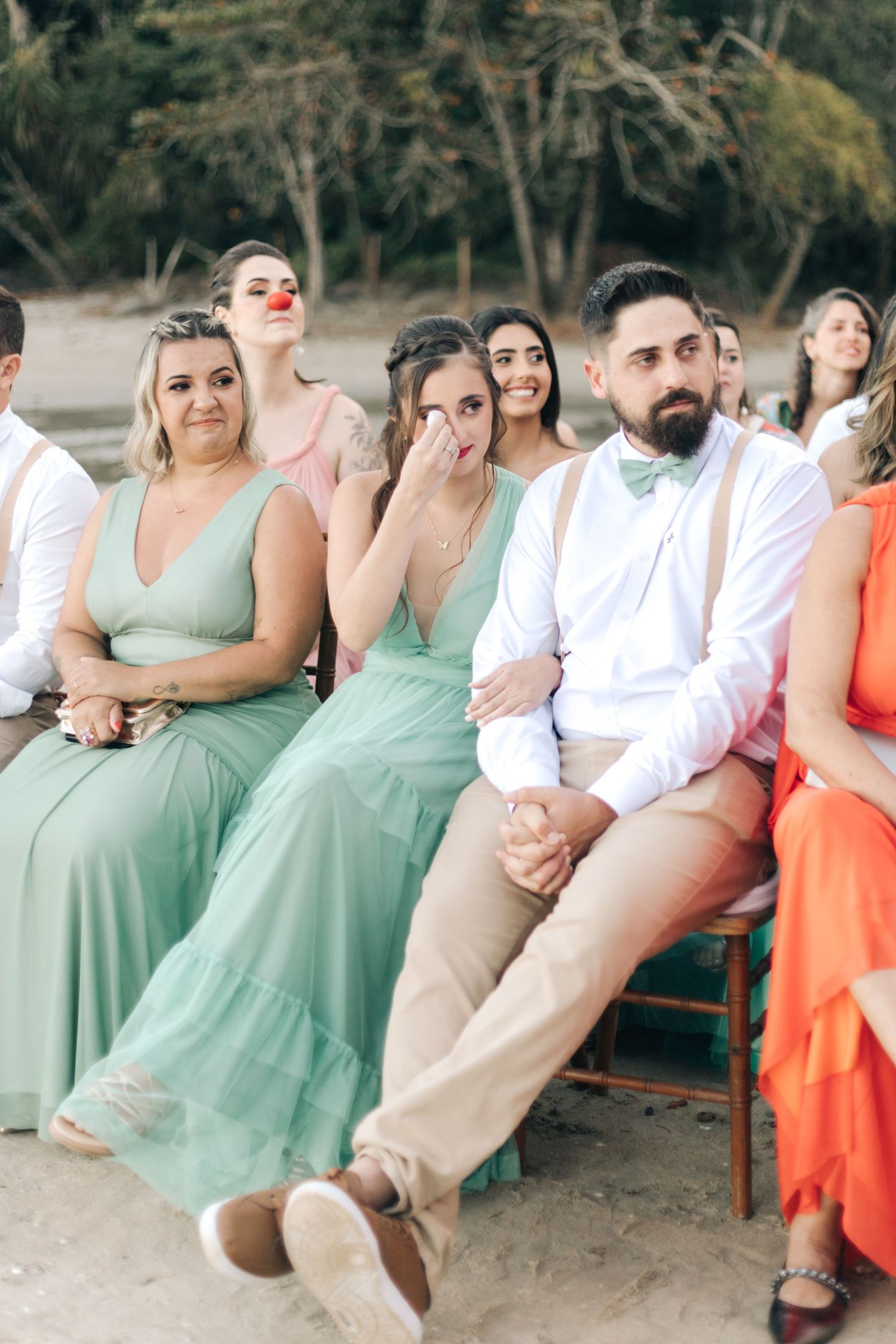 Wedding party seated in mint green and coral dresses during outdoor ceremony.