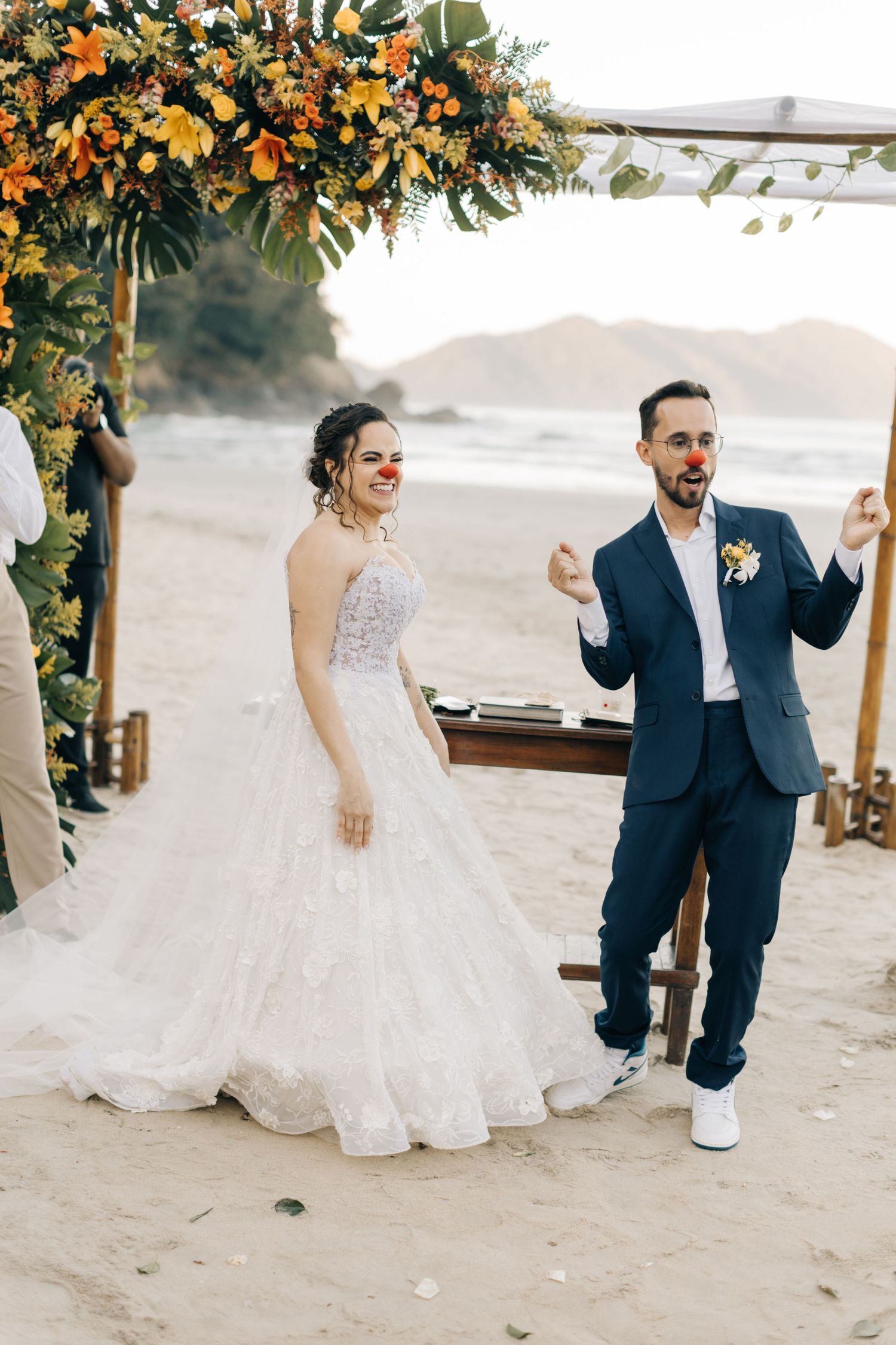 Festive moment during beach wedding ceremony under tropical flower arch with ocean view.