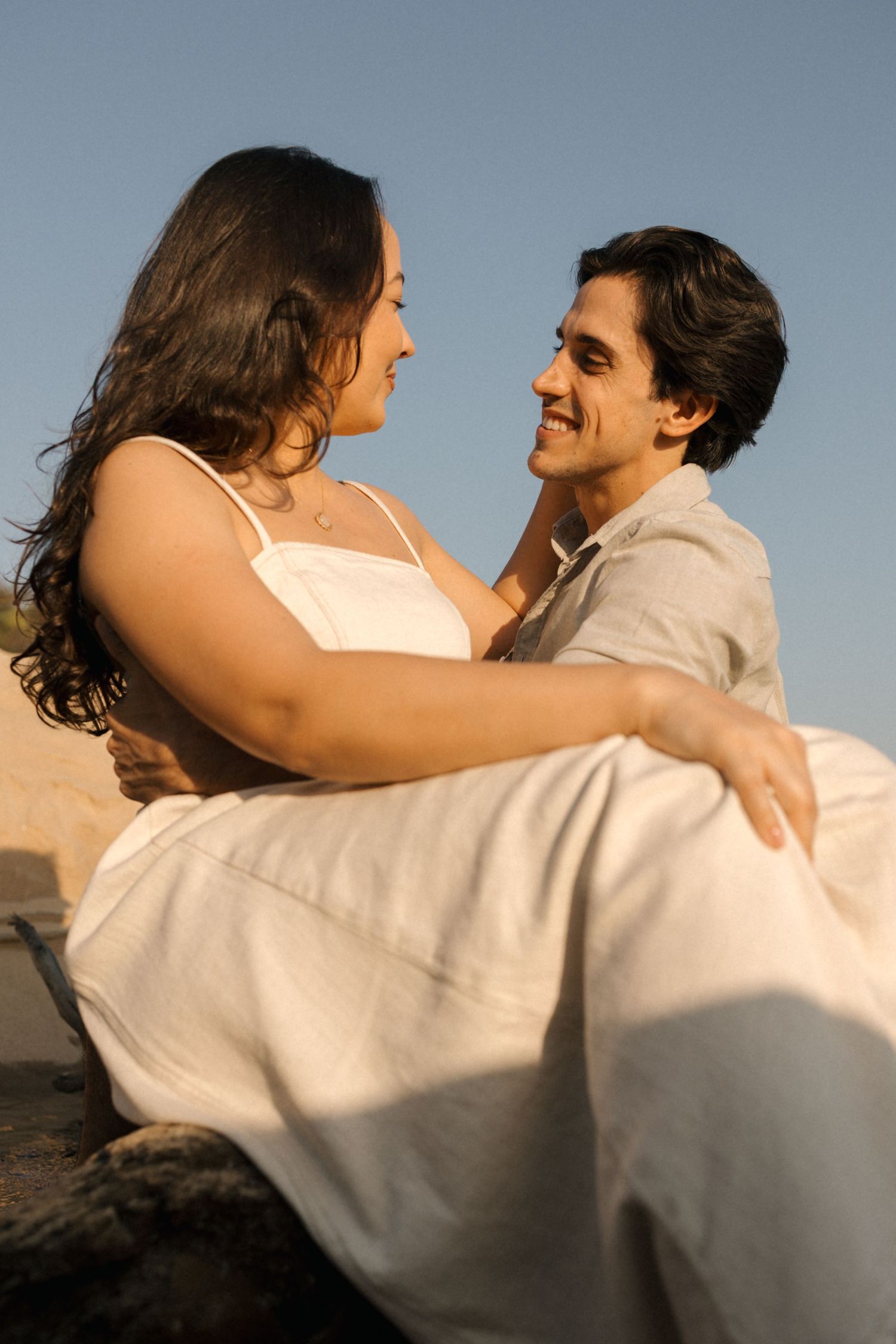 Couple in white embracing and dancing together on beach during golden hour.