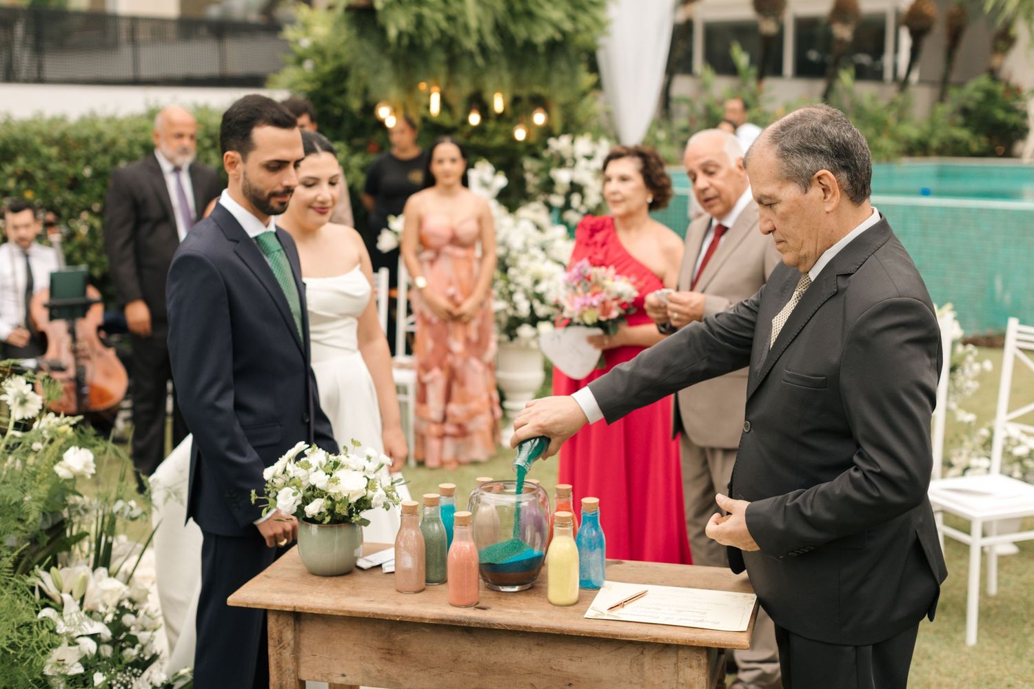 Wedding guests gather around a rustic table during an outdoor ceremony with colorful drinks.