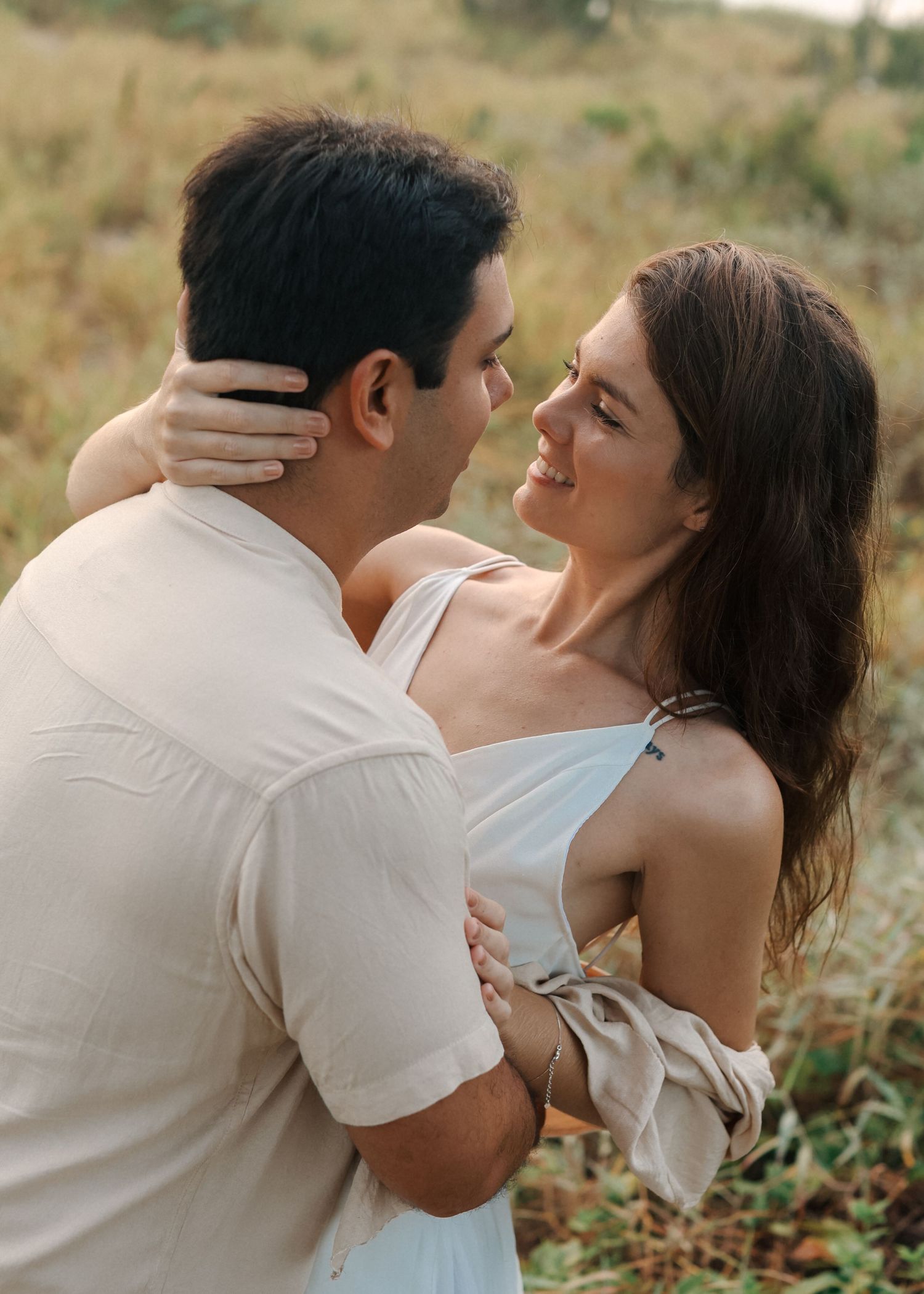 Couple in light colored outfits share tender moments during outdoor photoshoot.