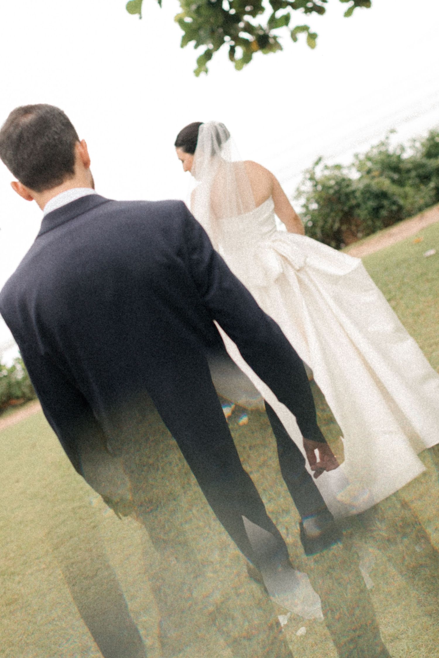 Back view of newlyweds walking together on a grassy hilltop overlooking the ocean.
