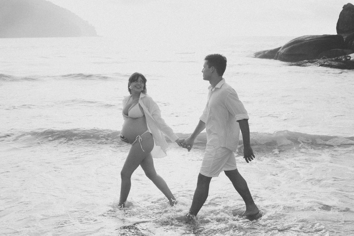 Playful couple running through ocean waves at the beach.