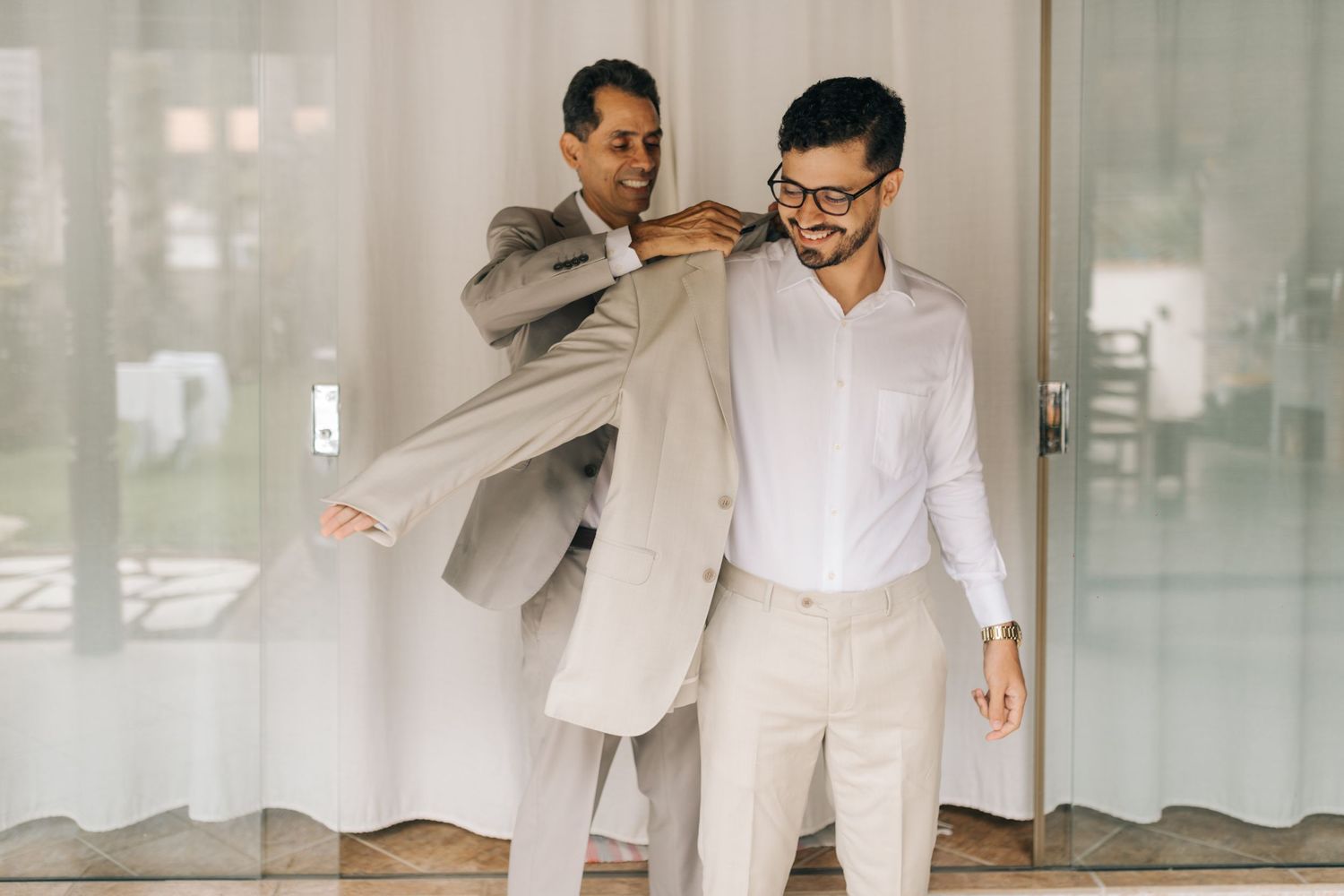 Two people in light colored suits during a formal dressing preparation.