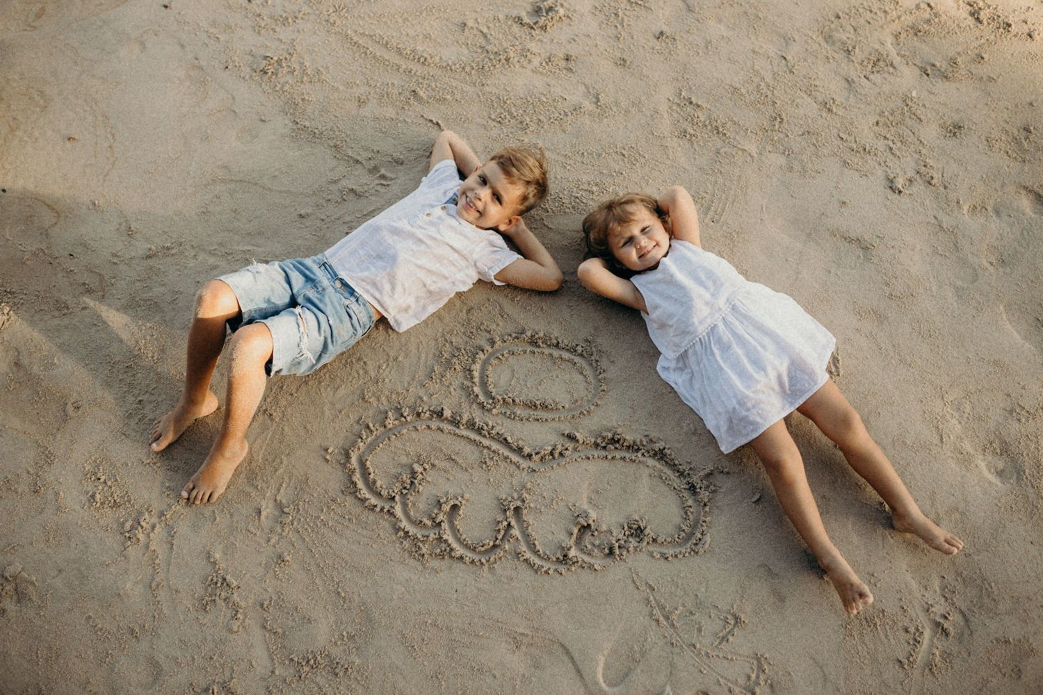 People lying on sandy beach making sand angels at sunset.