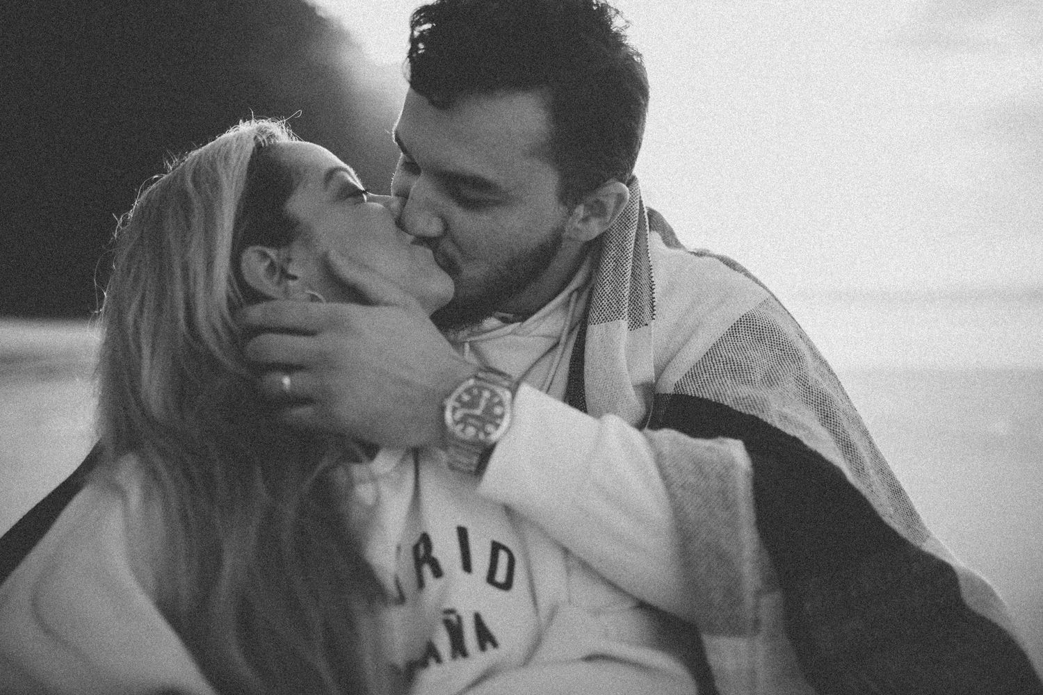 A couple sharing a passionate kiss while wrapped in a blanket on the beach.