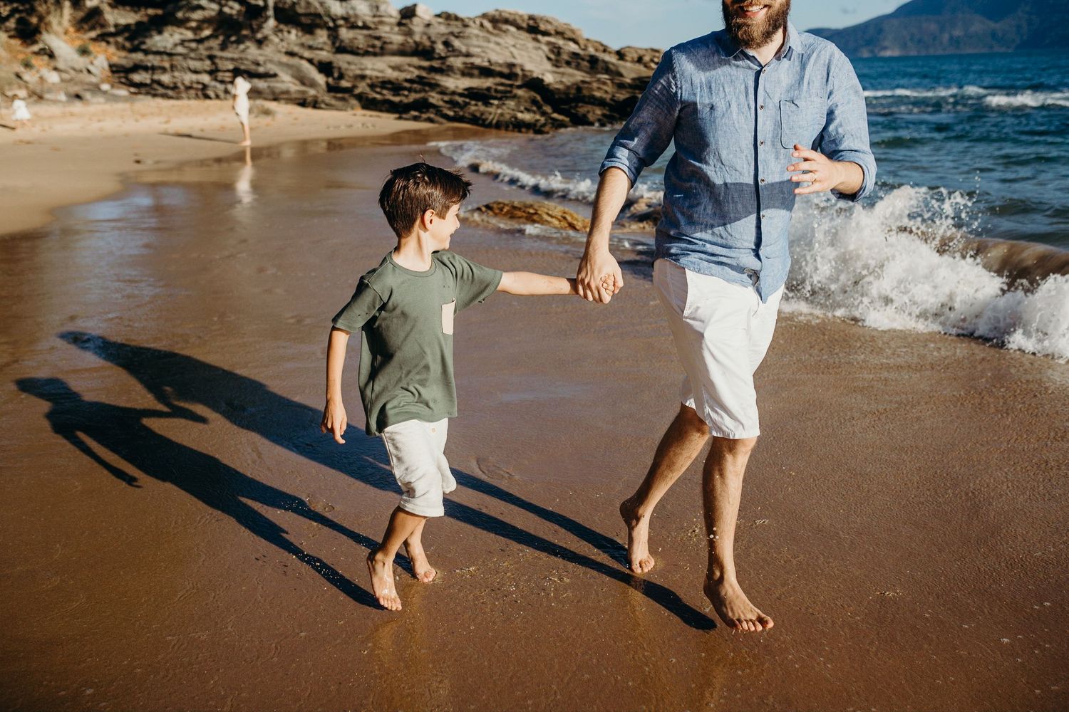Family walking and splashing in shallow ocean waves on sandy beach.