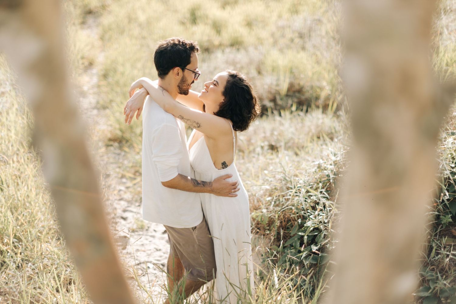 Romantic couple in white clothing share an intimate moment amid sunlit golden fields.
