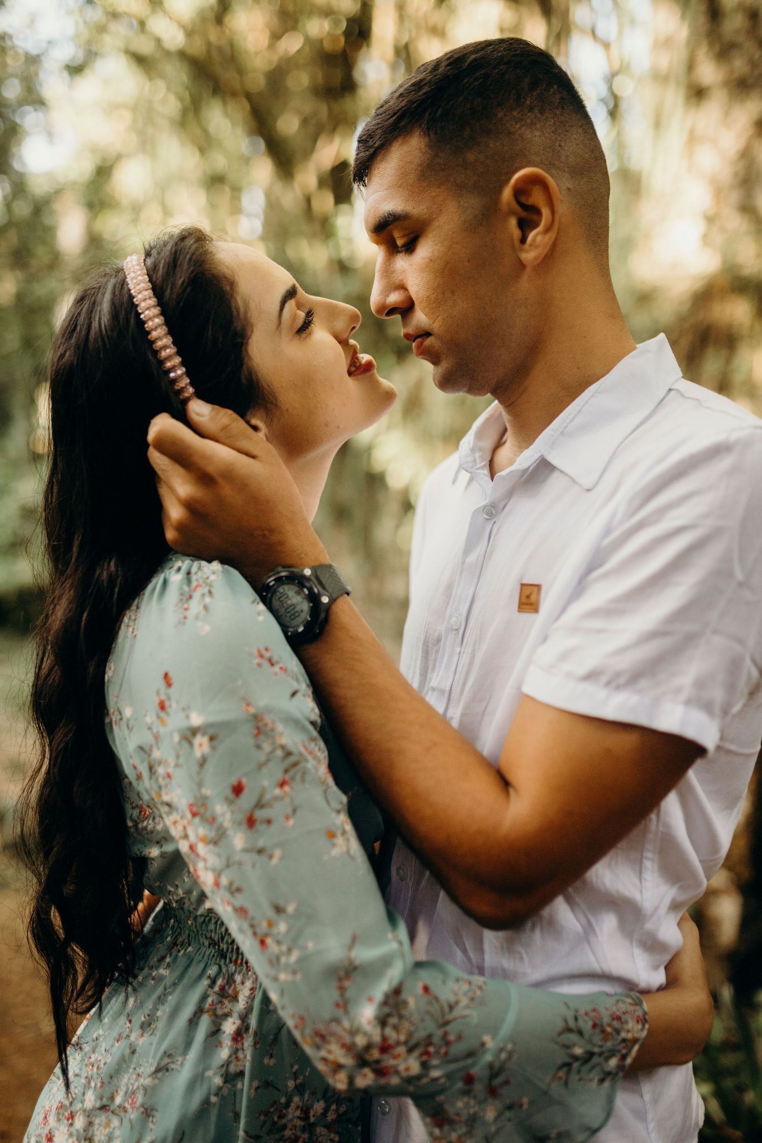 Couple in close embrace with soft natural lighting filtering through trees.