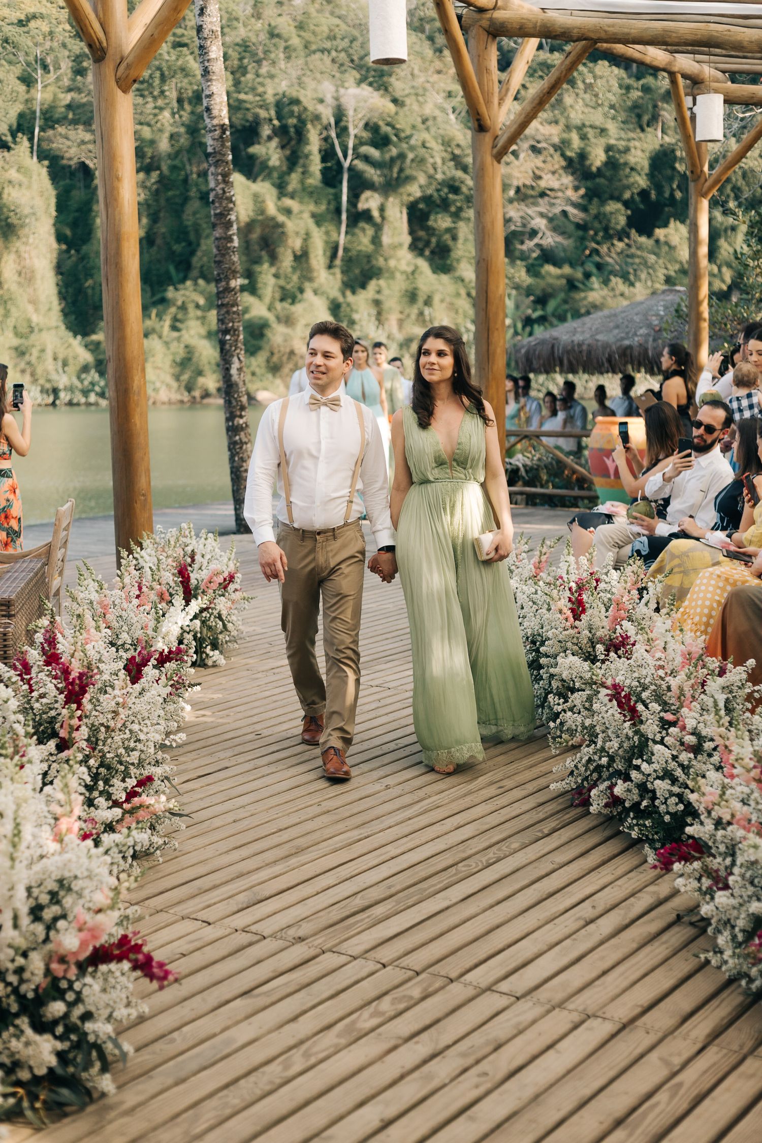 Couple strolling down flower-decorated wooden walkway with mountain backdrop.