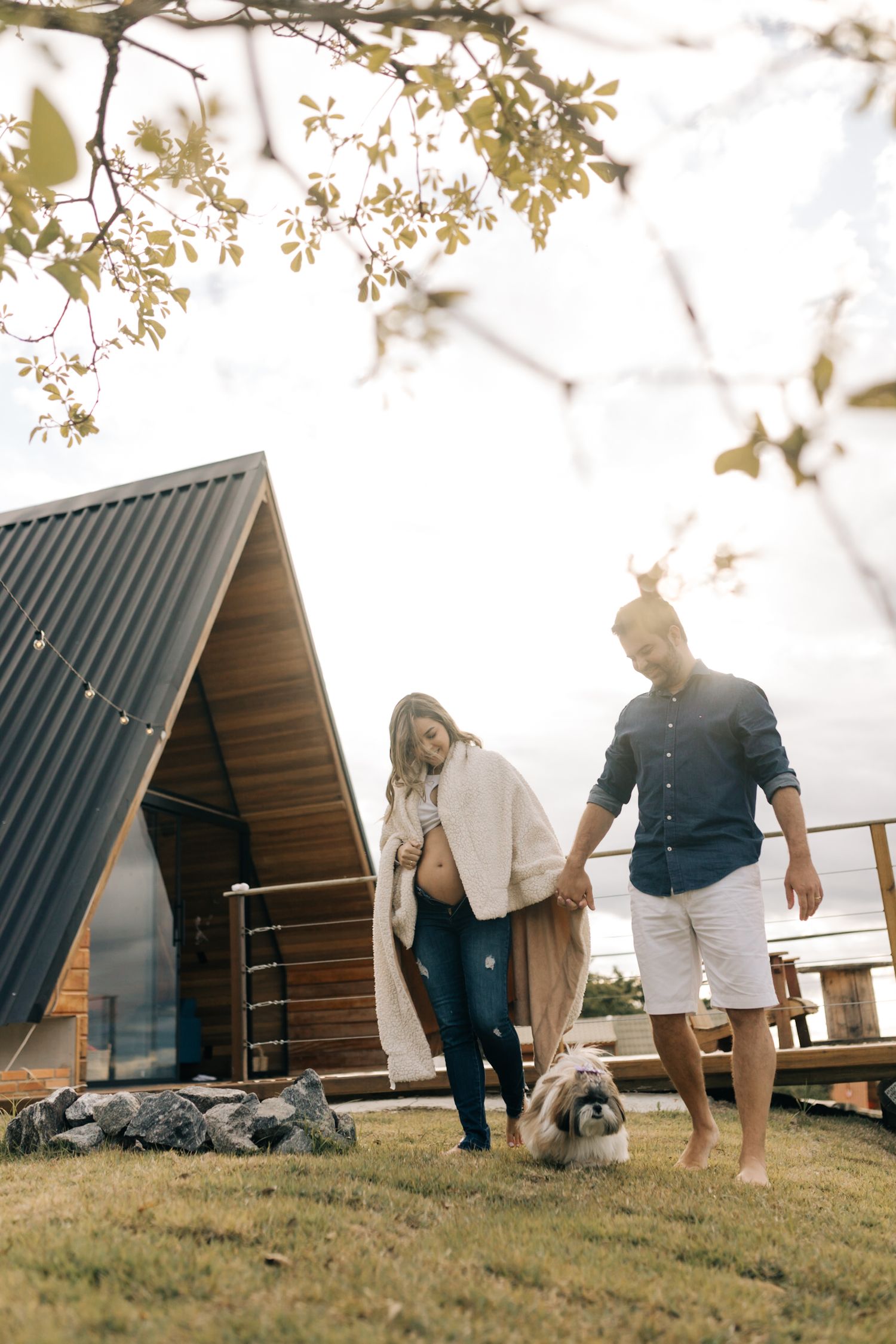 Casual outdoor maternity session with a dog at a rustic A-frame cabin in nature.
