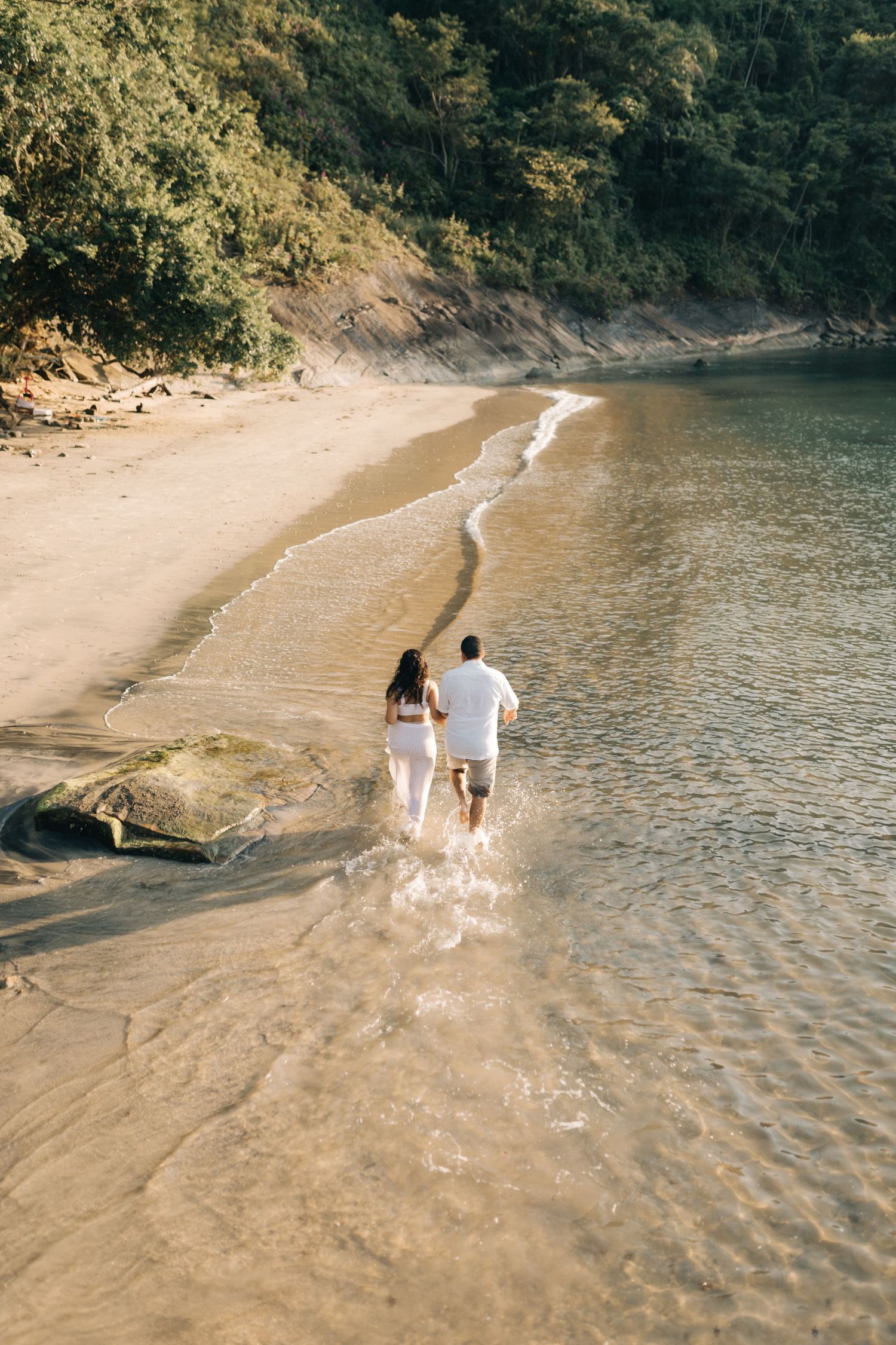 Romantic couple walks together along secluded beach shoreline surrounded by cliffs.