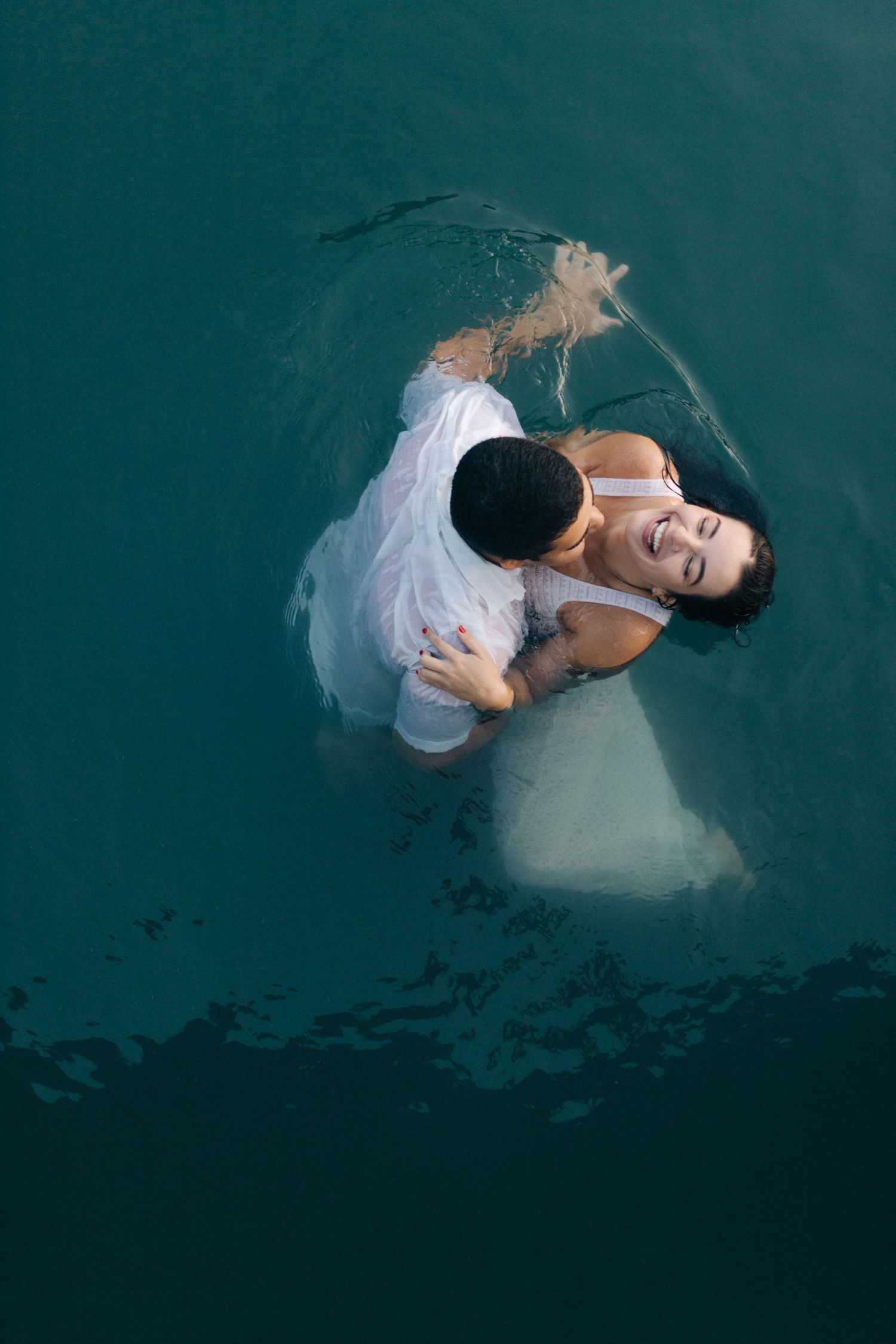 Figure in white dress floating gracefully in dark turquoise water creating artistic underwater motion.