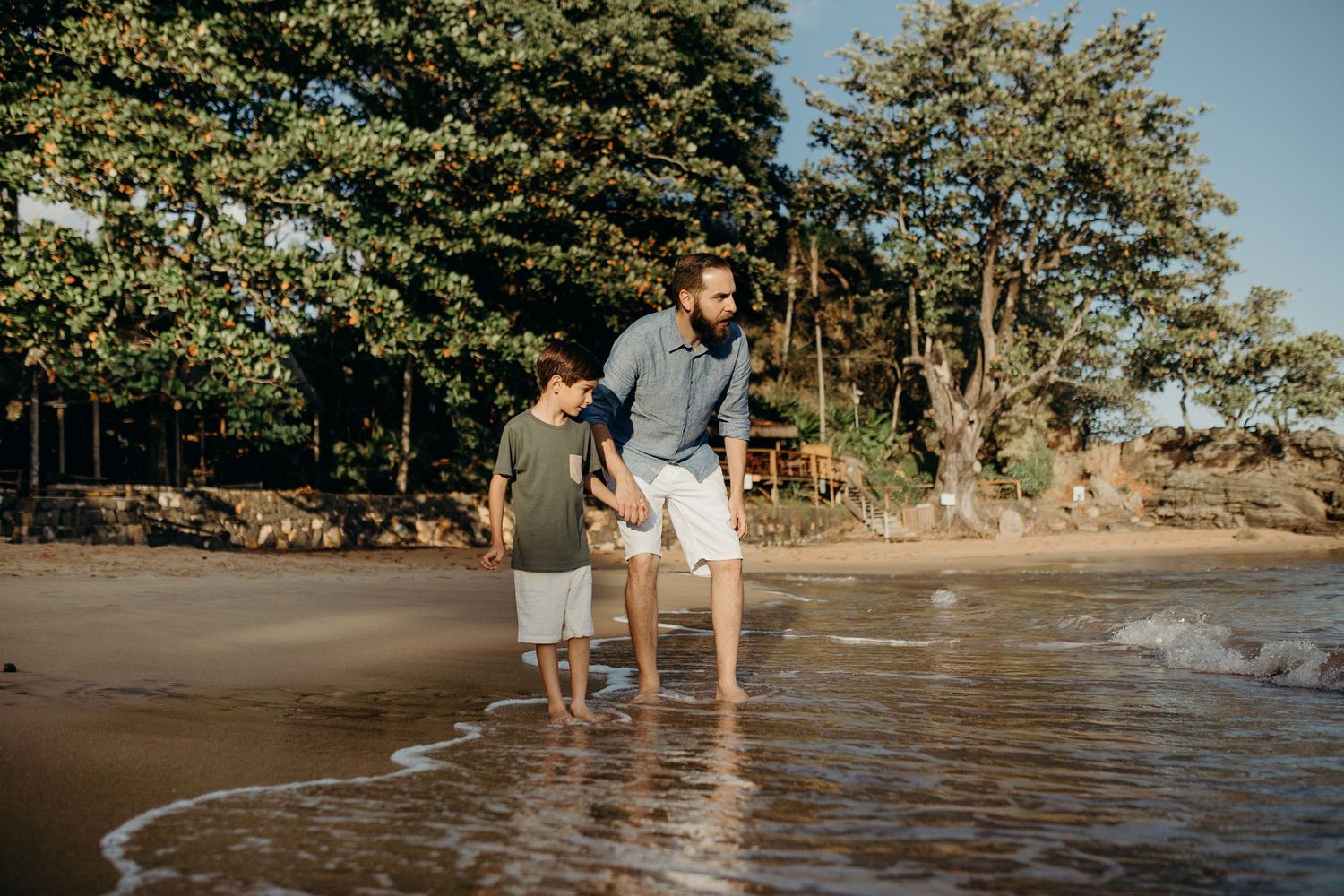 Two people enjoying the shoreline of a tropical beach with trees in background.